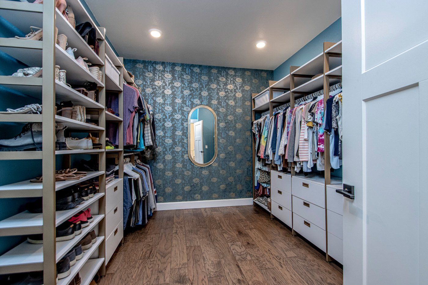 Spacious walk-in closet with built-in shelves, hanging space, and stylish wallpaper.