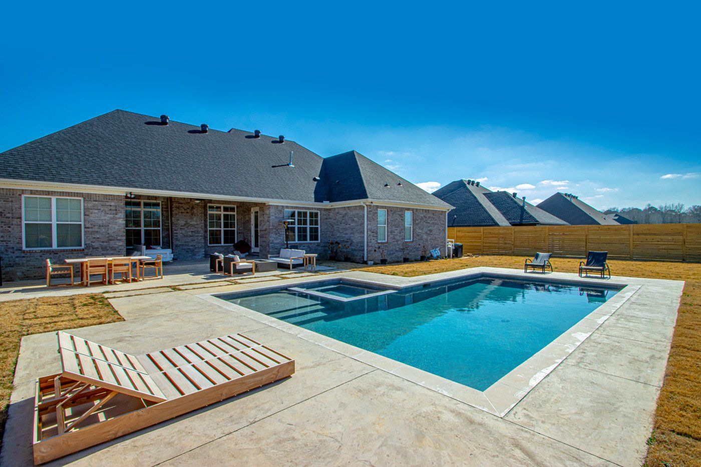 Backyard patio with pool, fire pit, and seating area in front of a modern house.