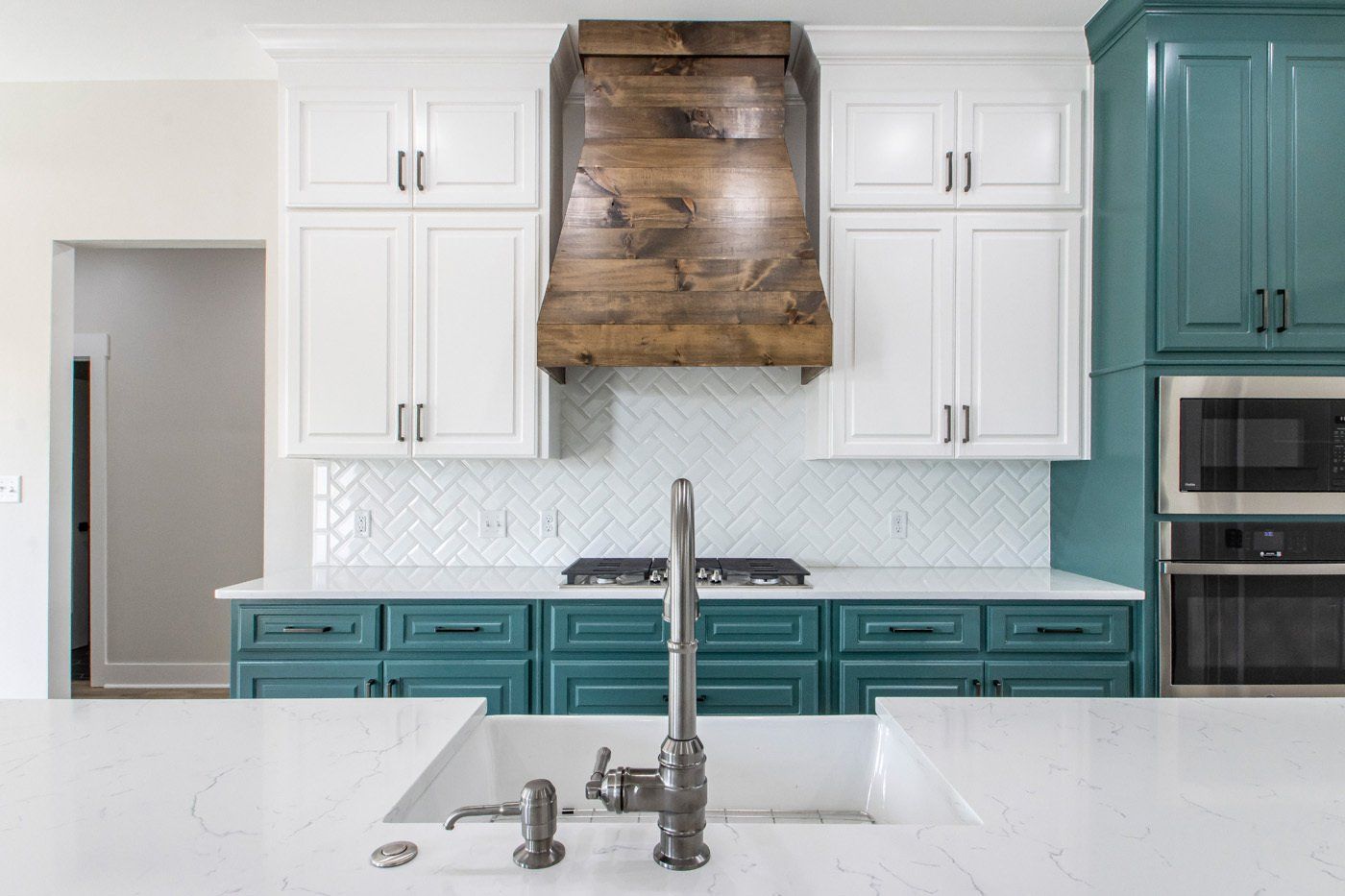 Bright kitchen featuring white and teal cabinetry, a wooden range hood, and modern countertops.