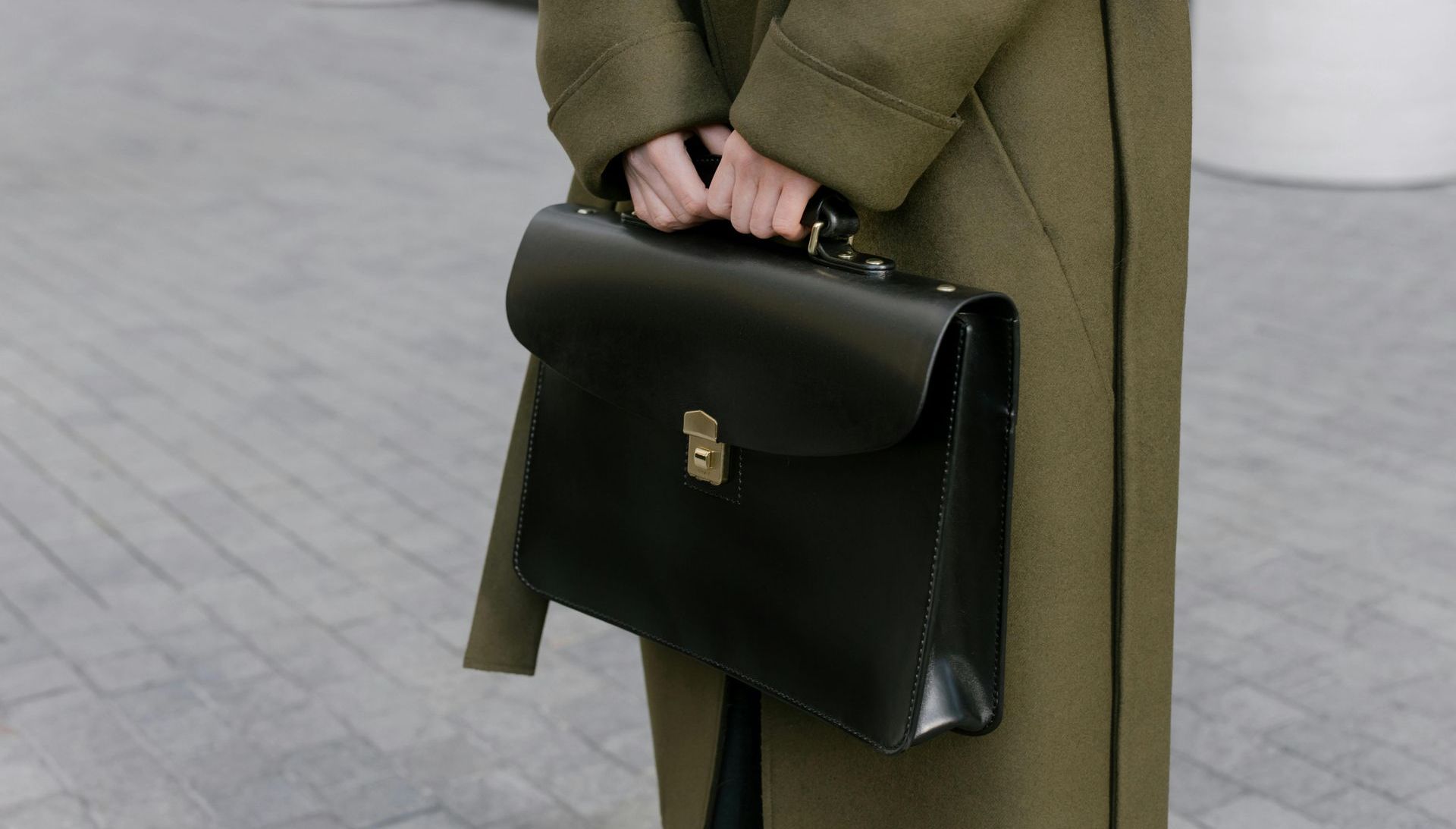 a woman in a green coat is holding a black briefcase.