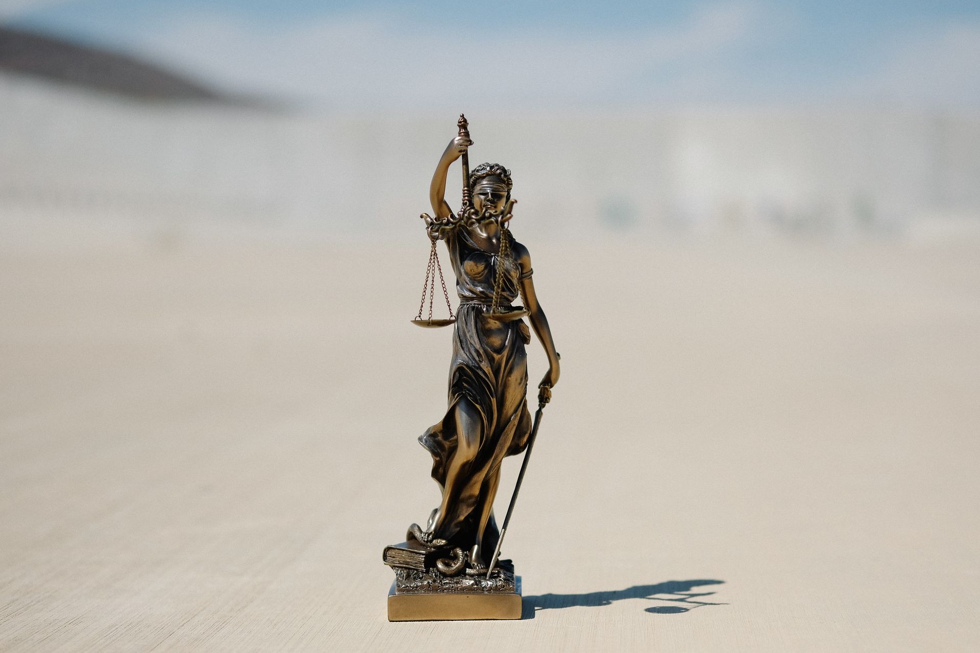 A statue of justice is standing in the sand holding scales of justice.