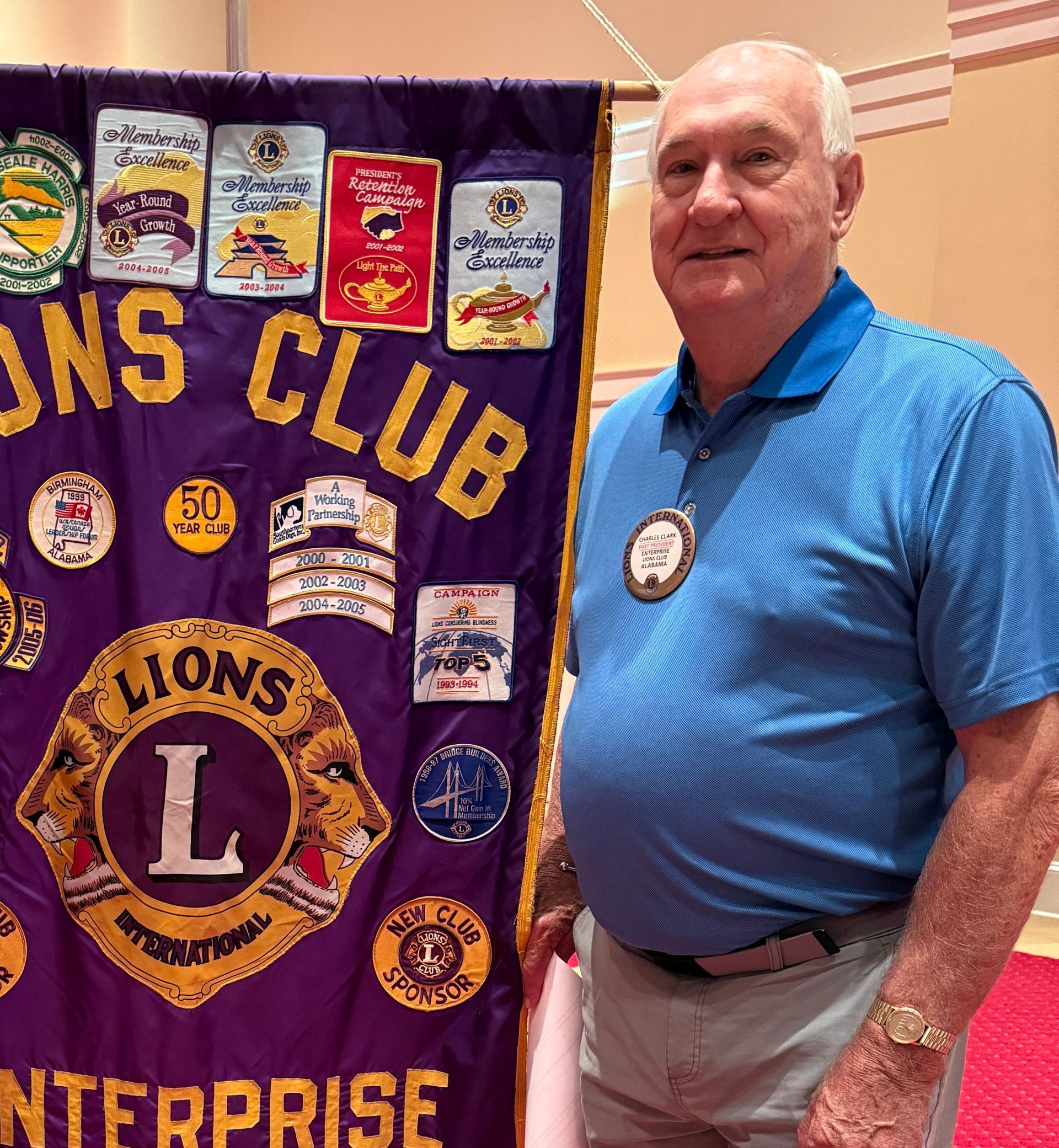 Man in blue shirt stands next to a purple Lions Club banner.