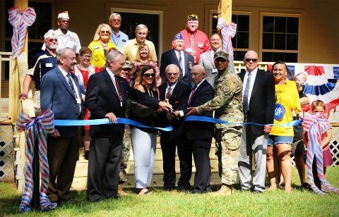 Group of people cutting a blue ribbon, celebrating an event outdoors.