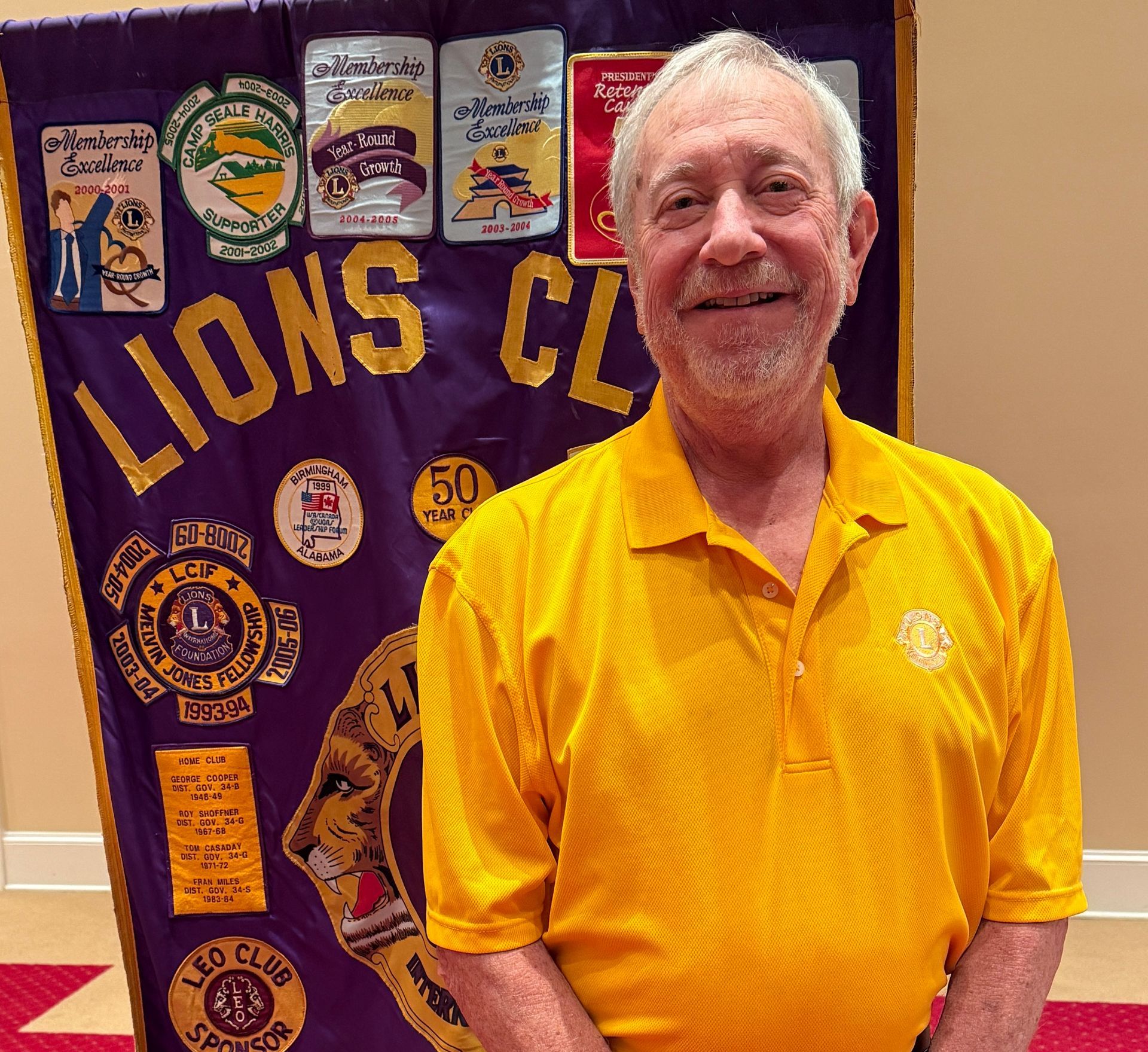 Man in yellow shirt stands in front of a Lions Club banner.