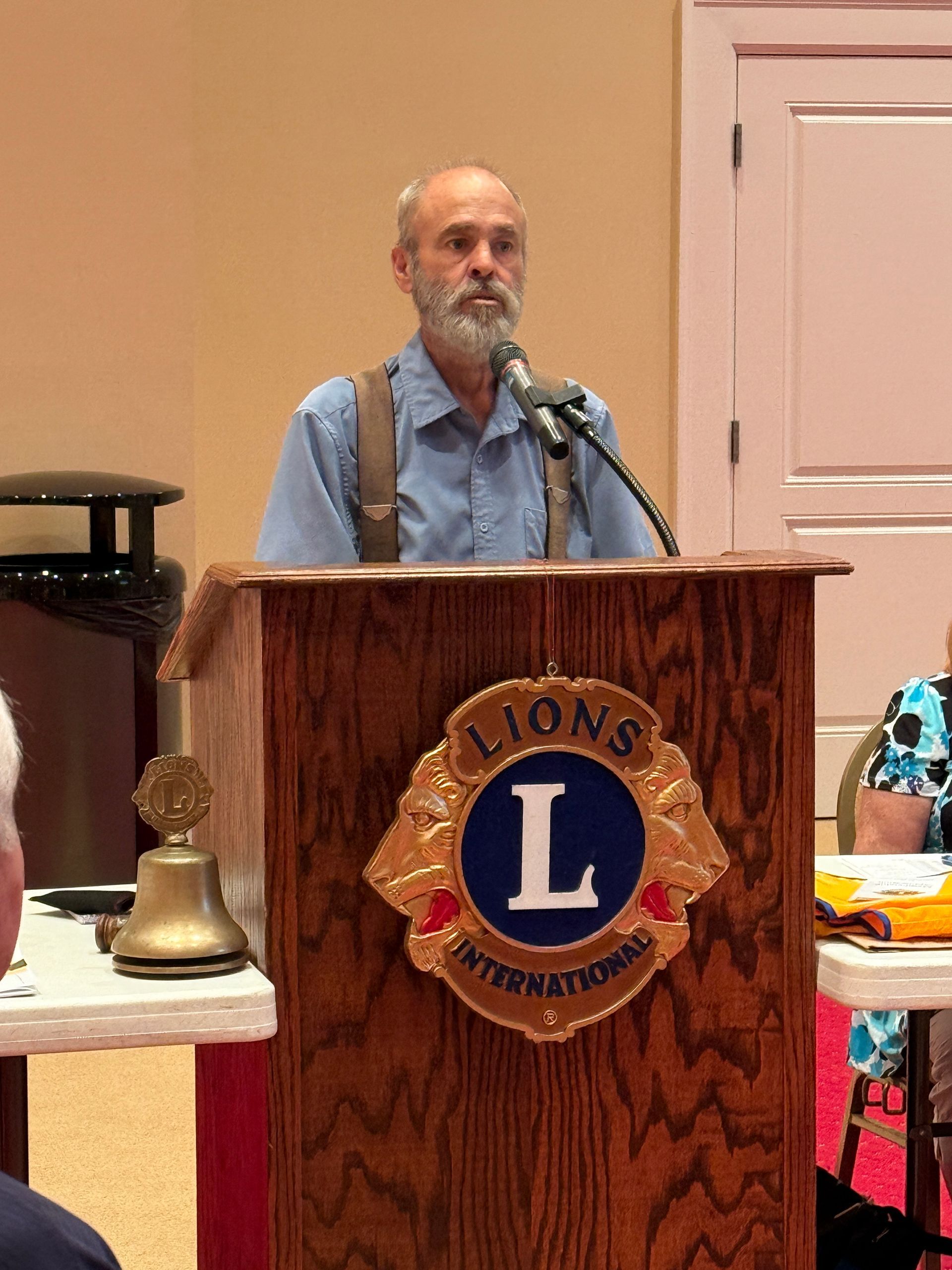 Man speaking at a Lions Club event behind a podium; the club's logo is visible.