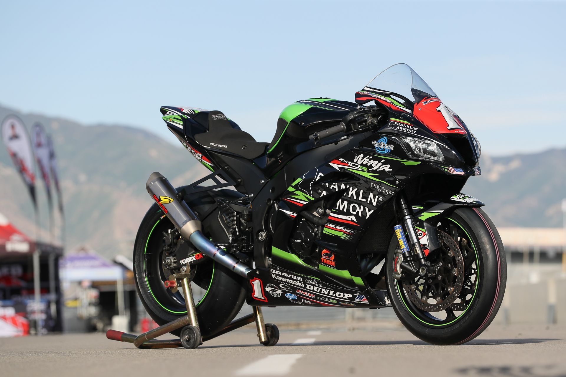 Kawasaki Ninja ZX-10R motorcycle with racing livery on a track, mountains in the background.