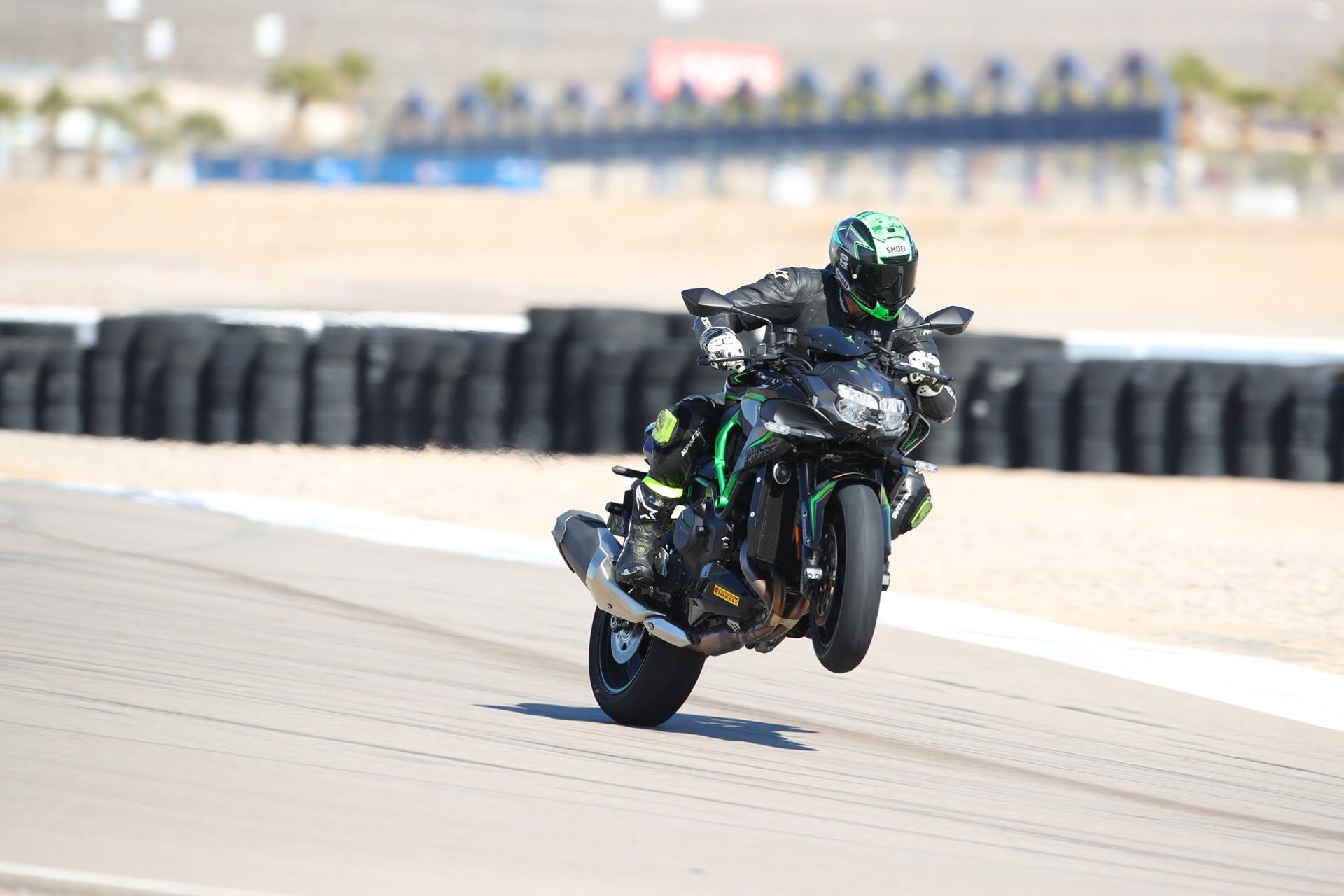 Motorcyclist on a green and black bike performing a wheelie on a racetrack.