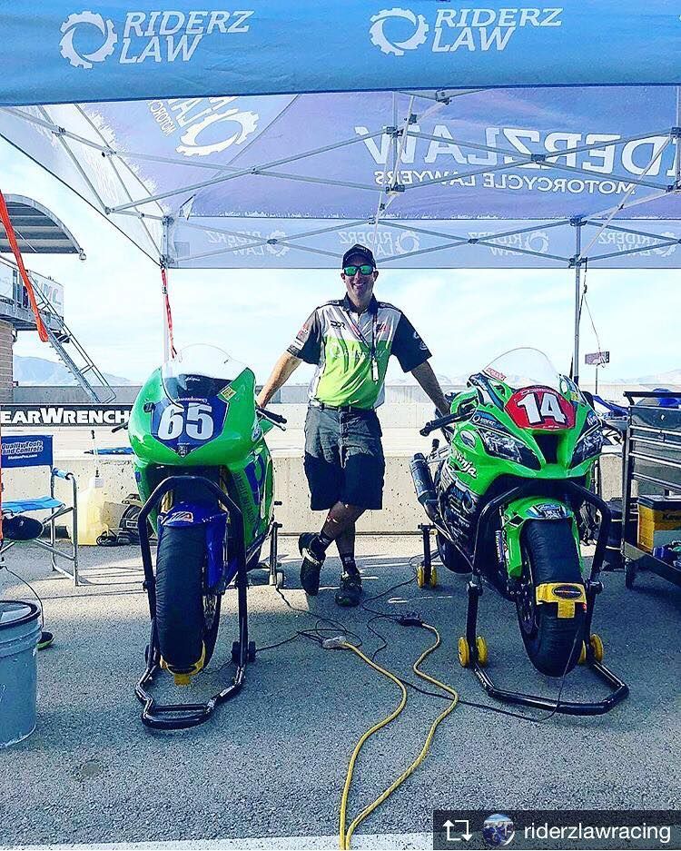 Man stands between two green motorcycles at a racetrack.