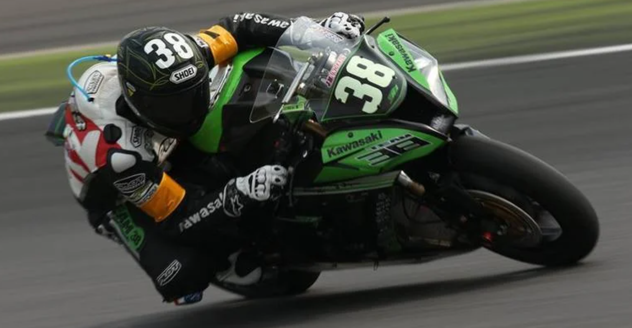 Motorcycle racer wearing helmet and gear, leaning into turn on black and green Kawasaki, track.