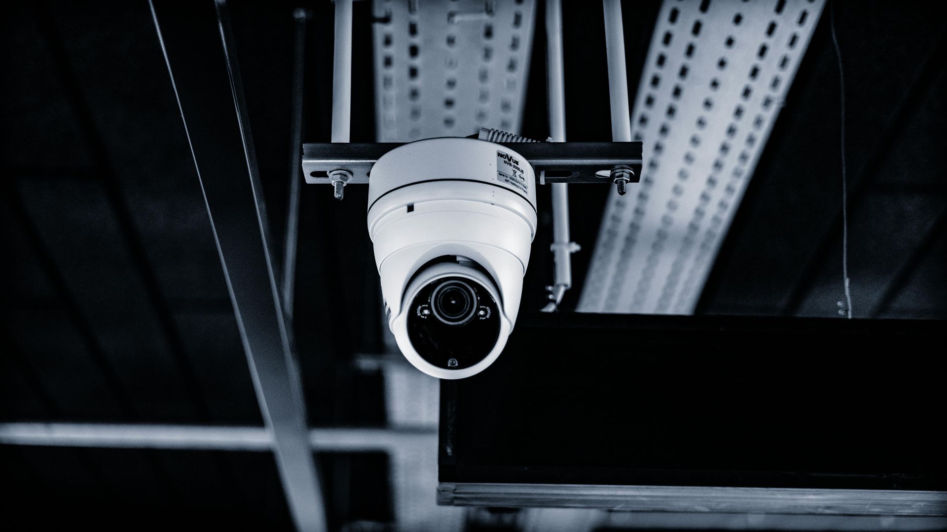 Security camera mounted on a ceiling, capturing a surveillance perspective in a dimly lit indoor space.