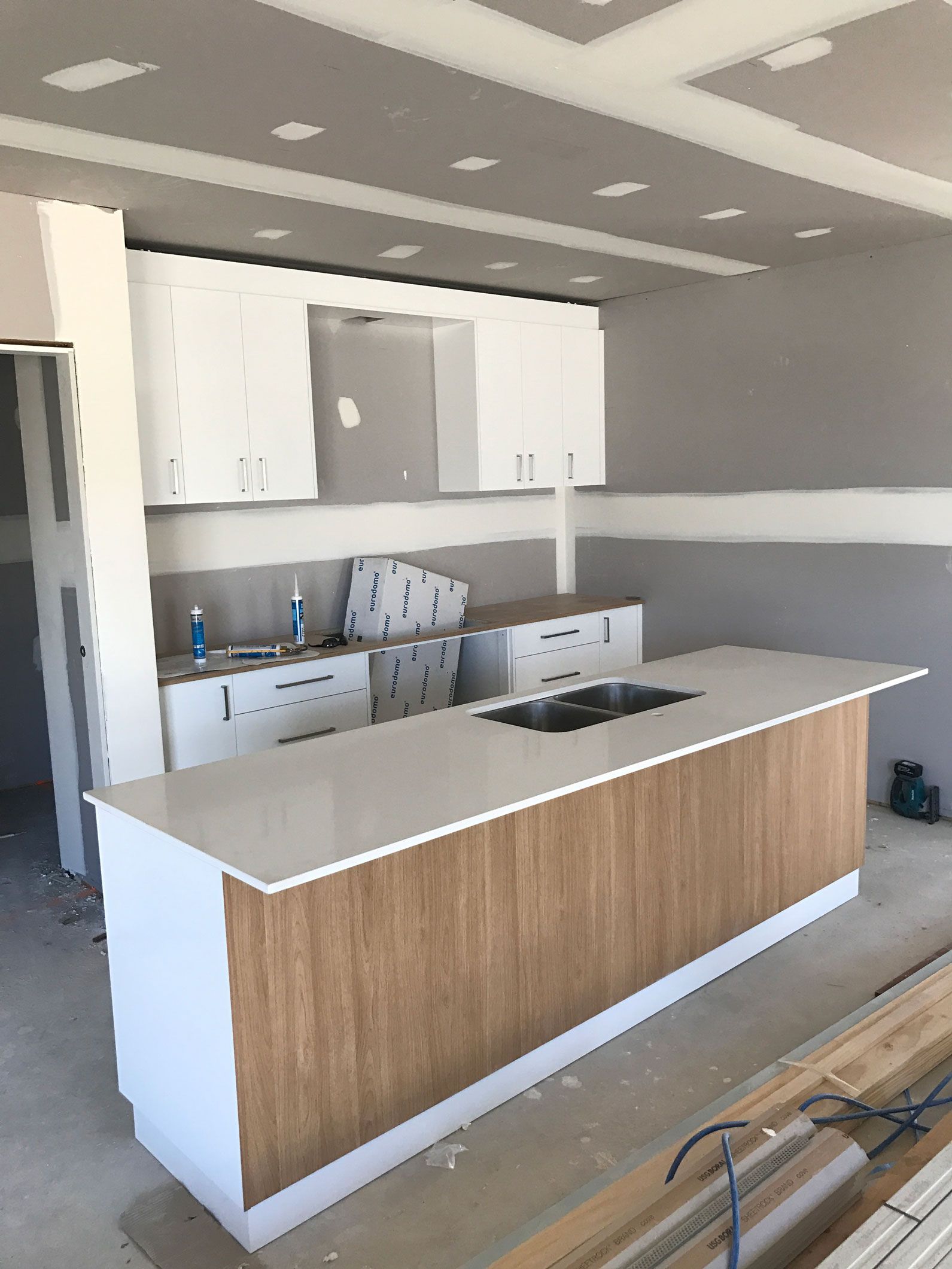 Kitchen under construction with white cabinets, light wood island, and gray walls.