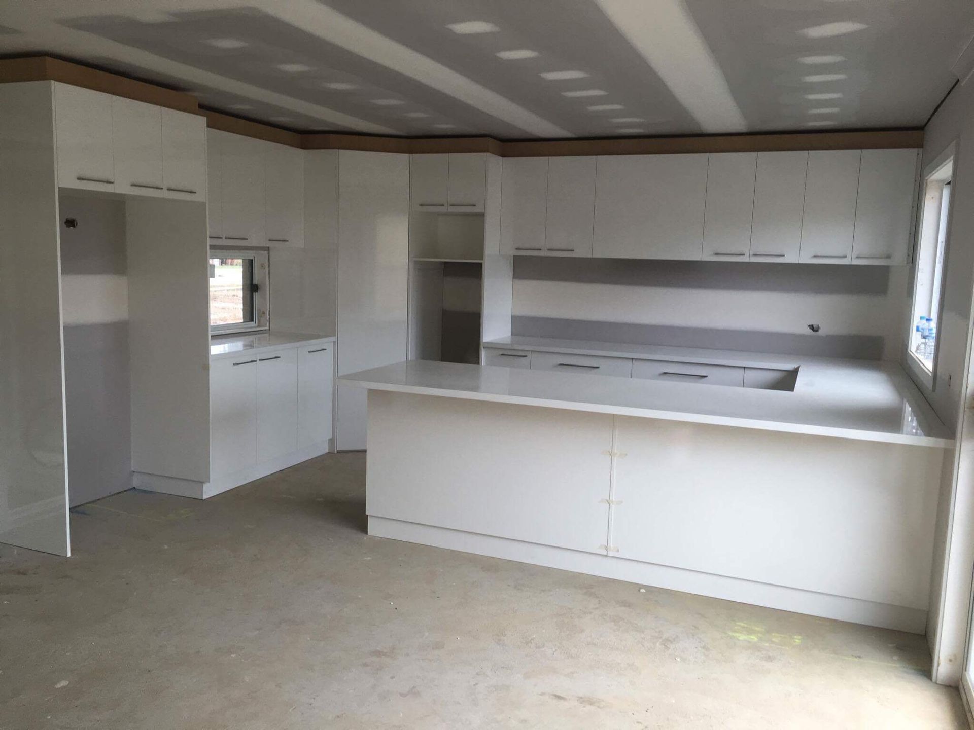 White kitchen cabinets and countertops in a room under construction.