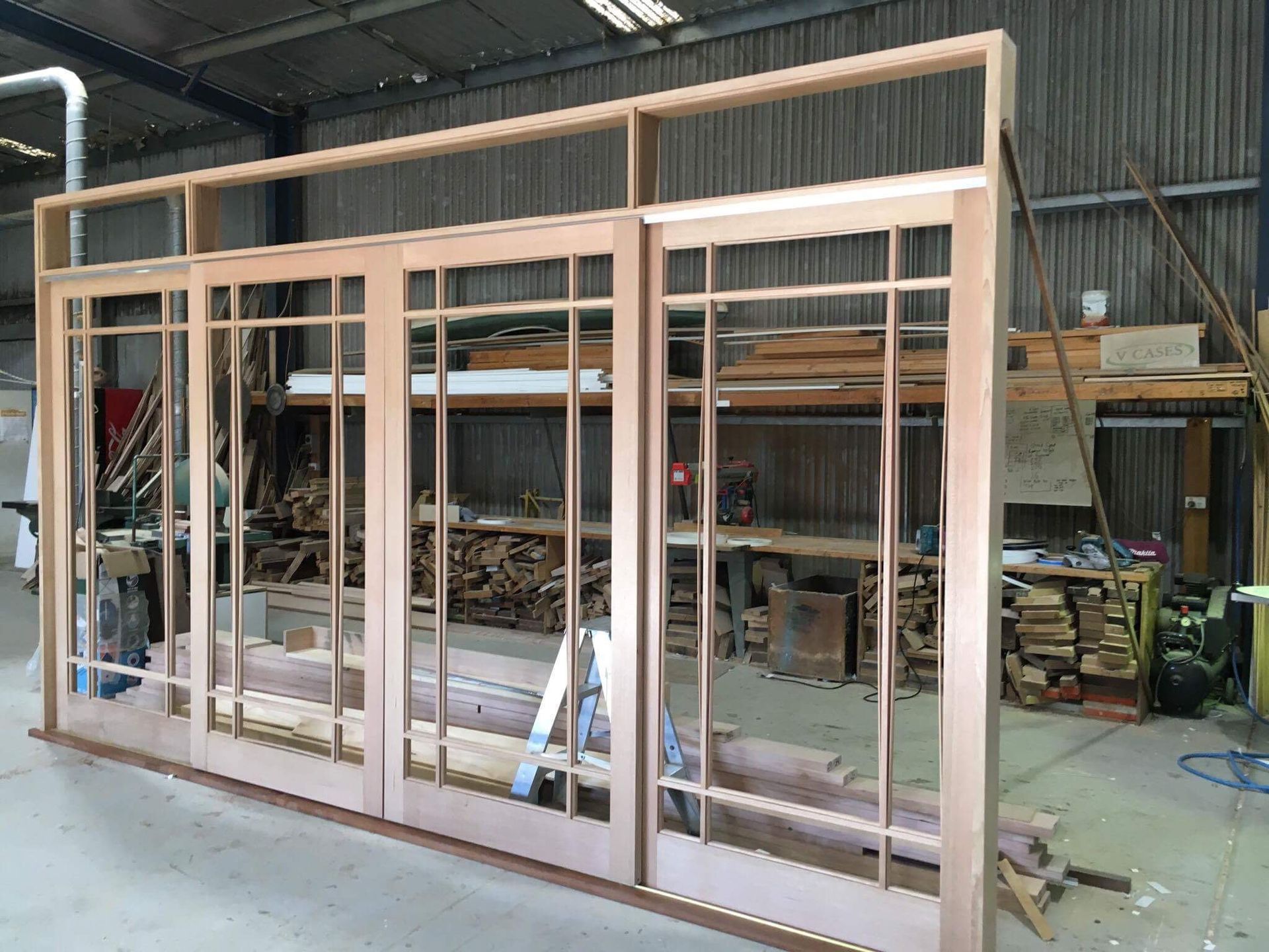 Wooden window frame assembly in a workshop, showcasing a grid-style design with multiple panes.