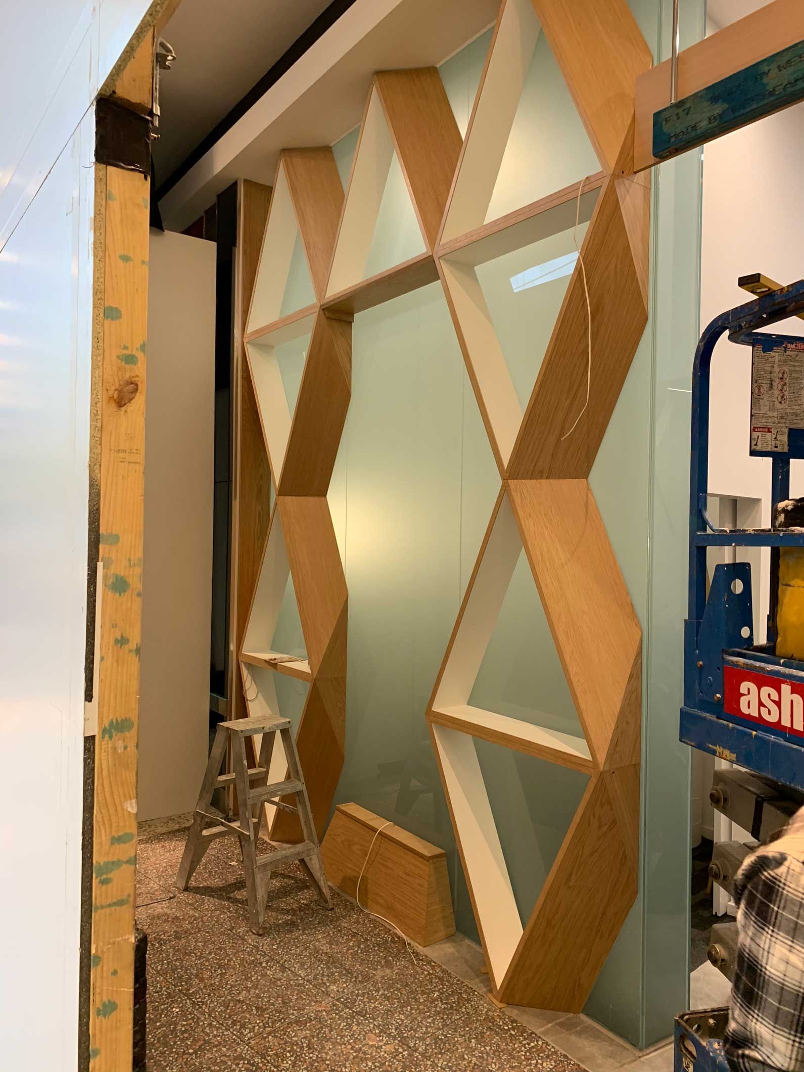 Geometric wooden shelving with triangular and hexagonal shapes against a light green wall in a construction zone.
