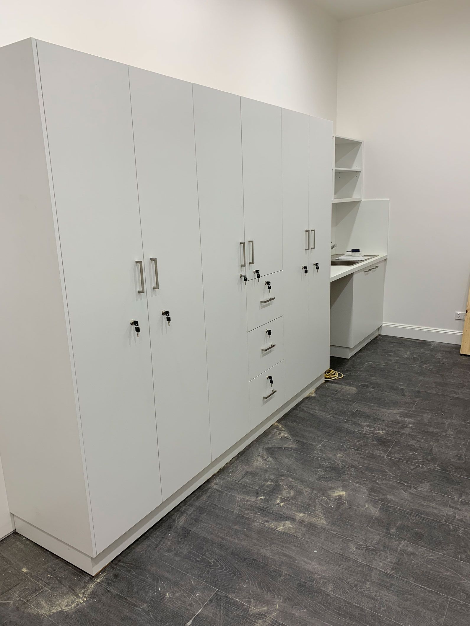 Gray cabinets and shelves against a white wall in a room with a dark gray floor.