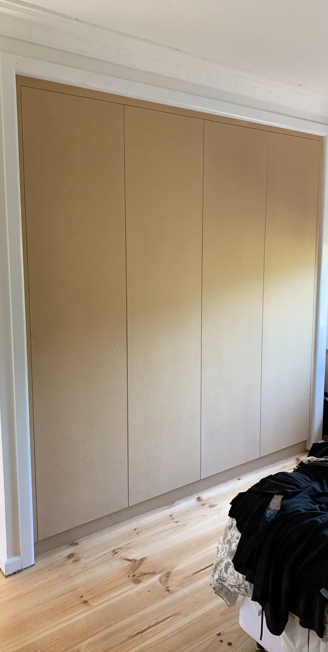 A wall covered in light brown panels. The panels are next to each other. Wooden floor and a bed with a black blanket.