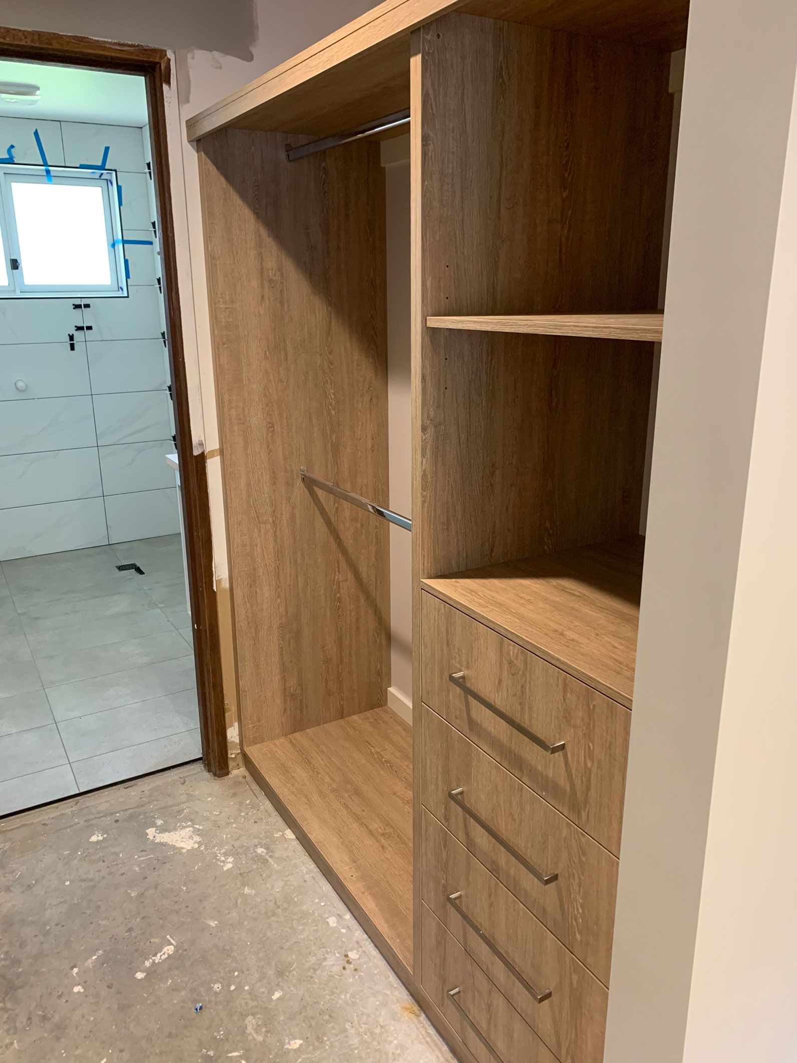 A built-in wooden closet with a hanging rod, shelves, and drawers. A doorway is to the left.
