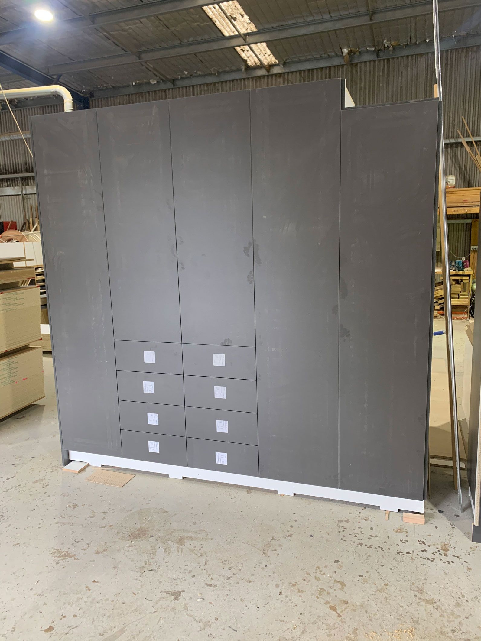 Large gray wall with cut-out squares and white baseboard, set in a warehouse.
