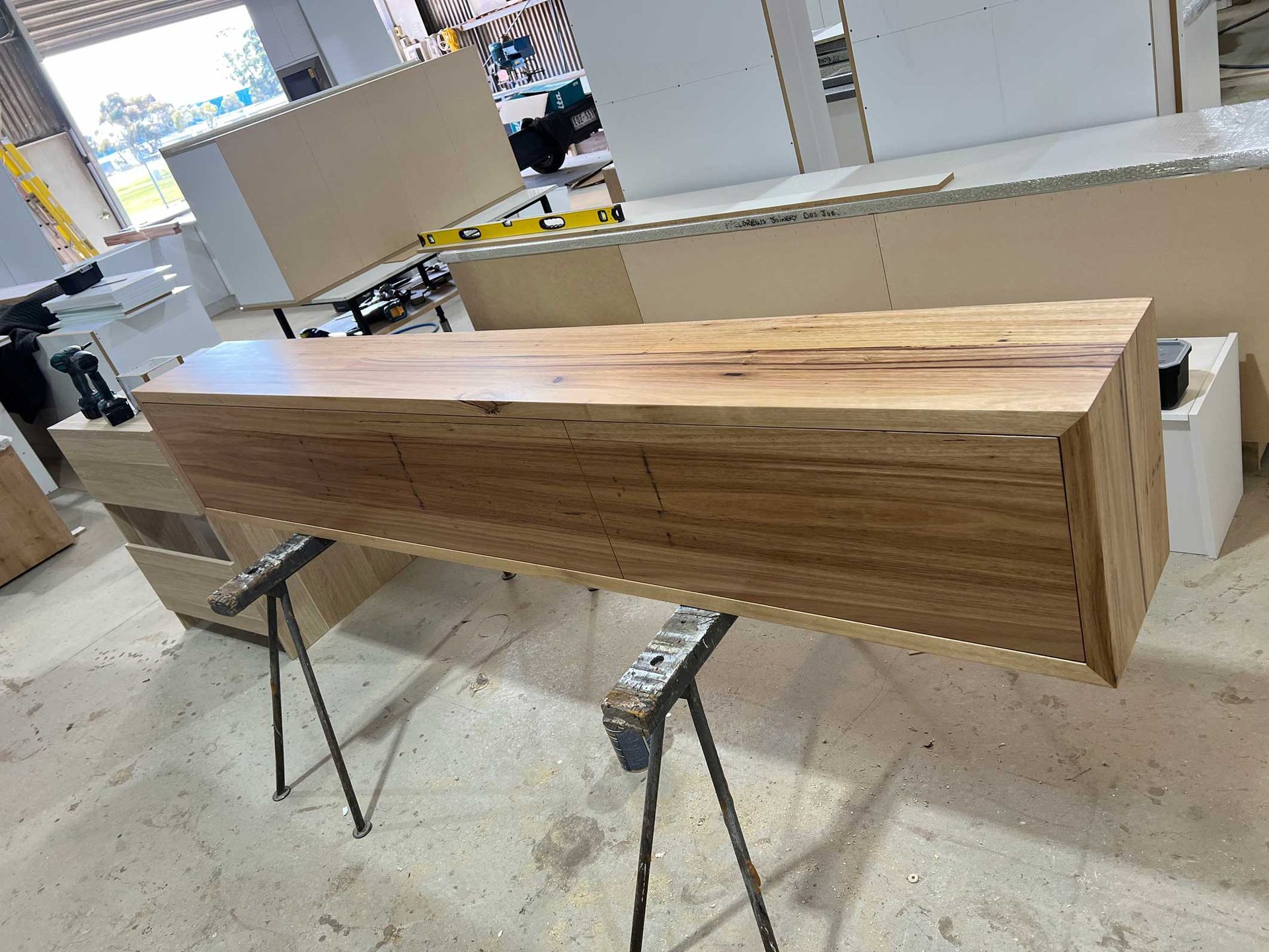 Wooden cabinet with two drawers on sawhorses in a workshop.