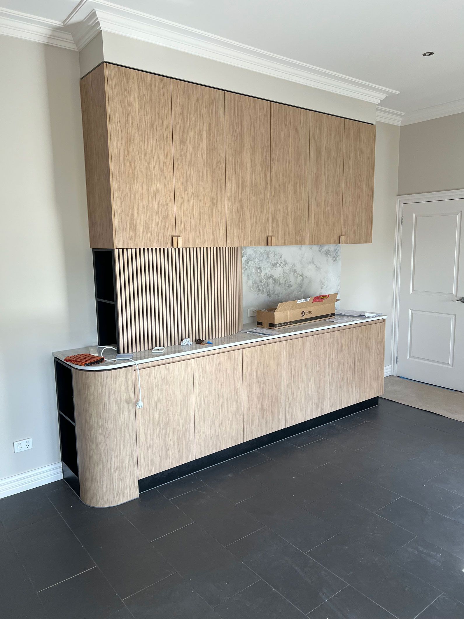Built-in plywood cabinetry with curved edges and a textured center section, in a room with dark flooring and crown molding.