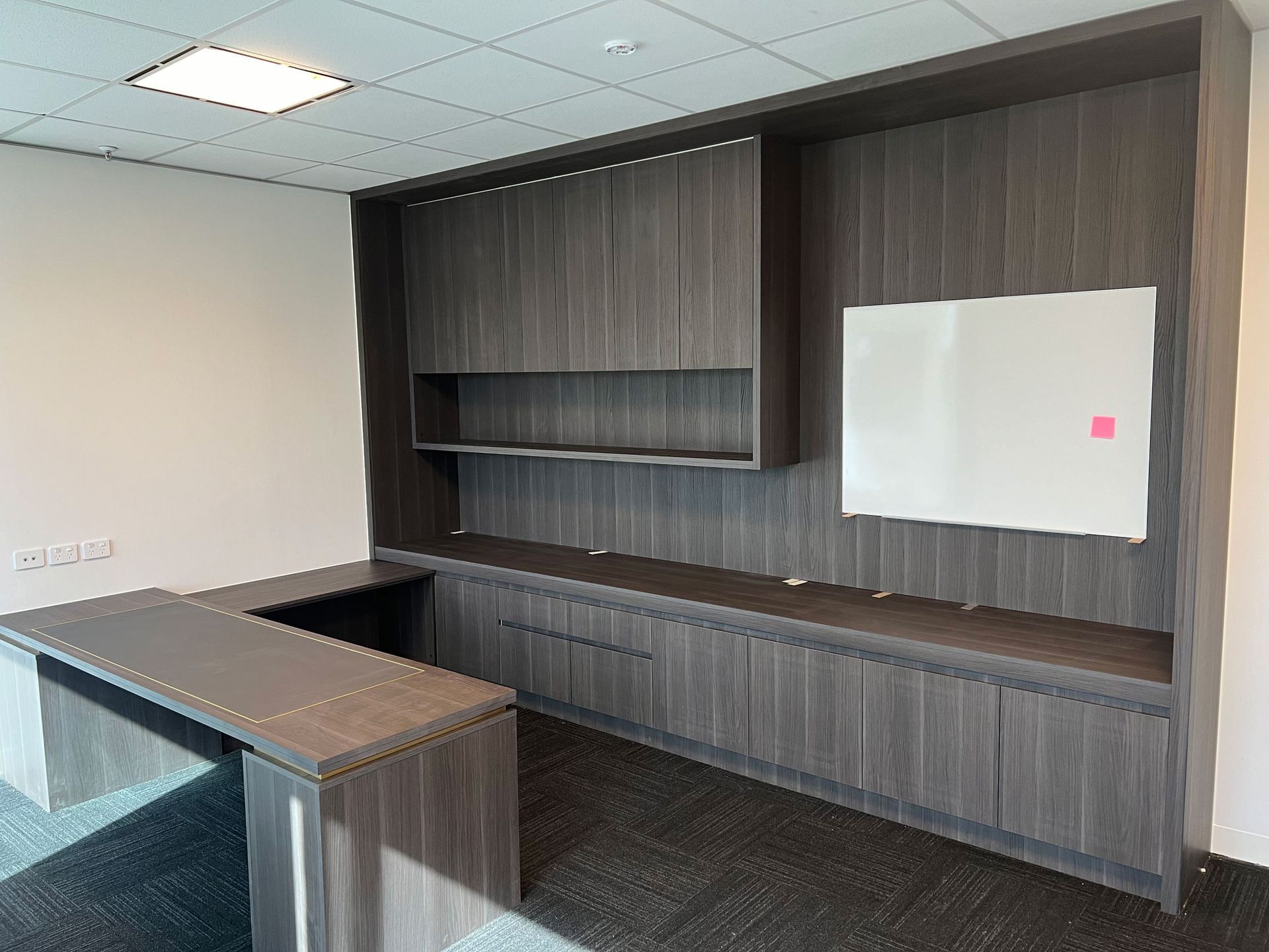 Empty office with dark wood cabinets, a whiteboard, and a gray desk.
