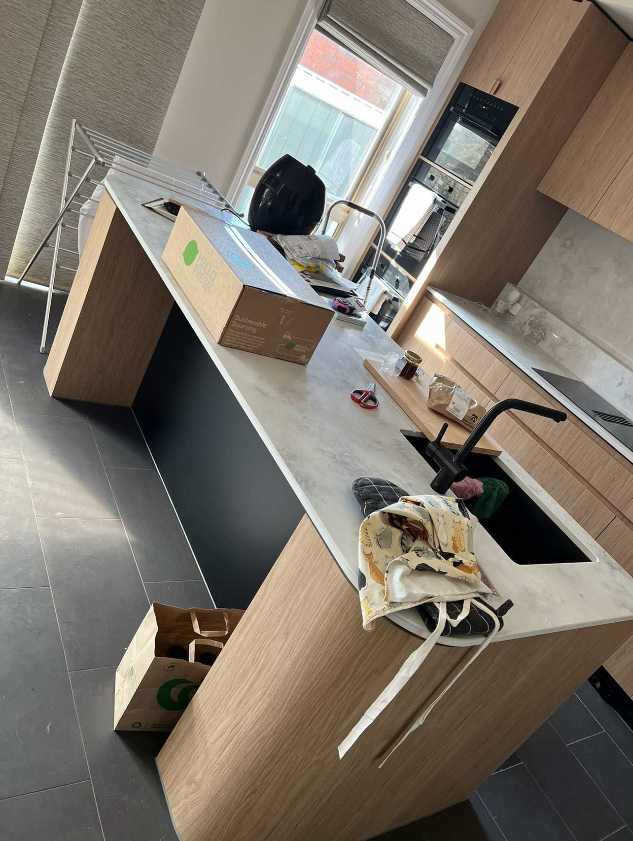 Kitchen island with light wood cabinets, light countertop, black sink, and a window.