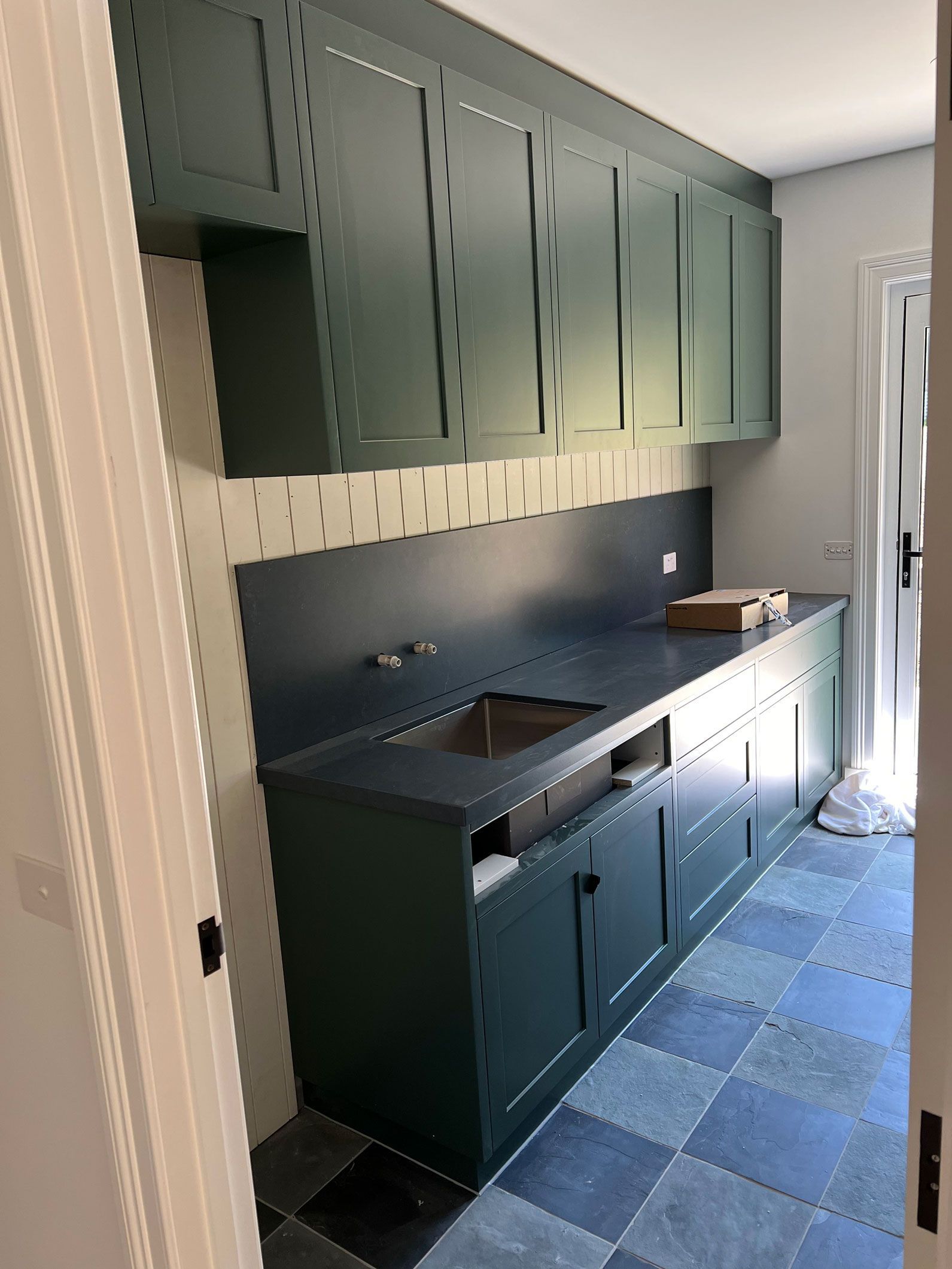 Green cabinets and countertop with a sink in a room with blue and white patterned floor tiles.
