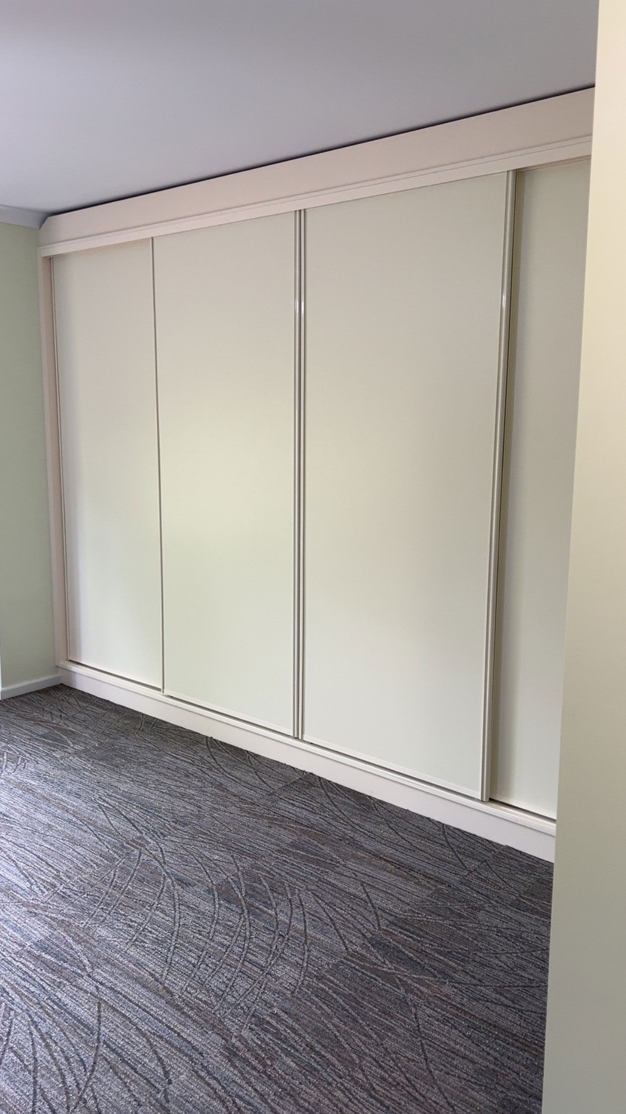 Closet with four sliding cream-colored doors, in a room with patterned gray carpet and a light green wall.