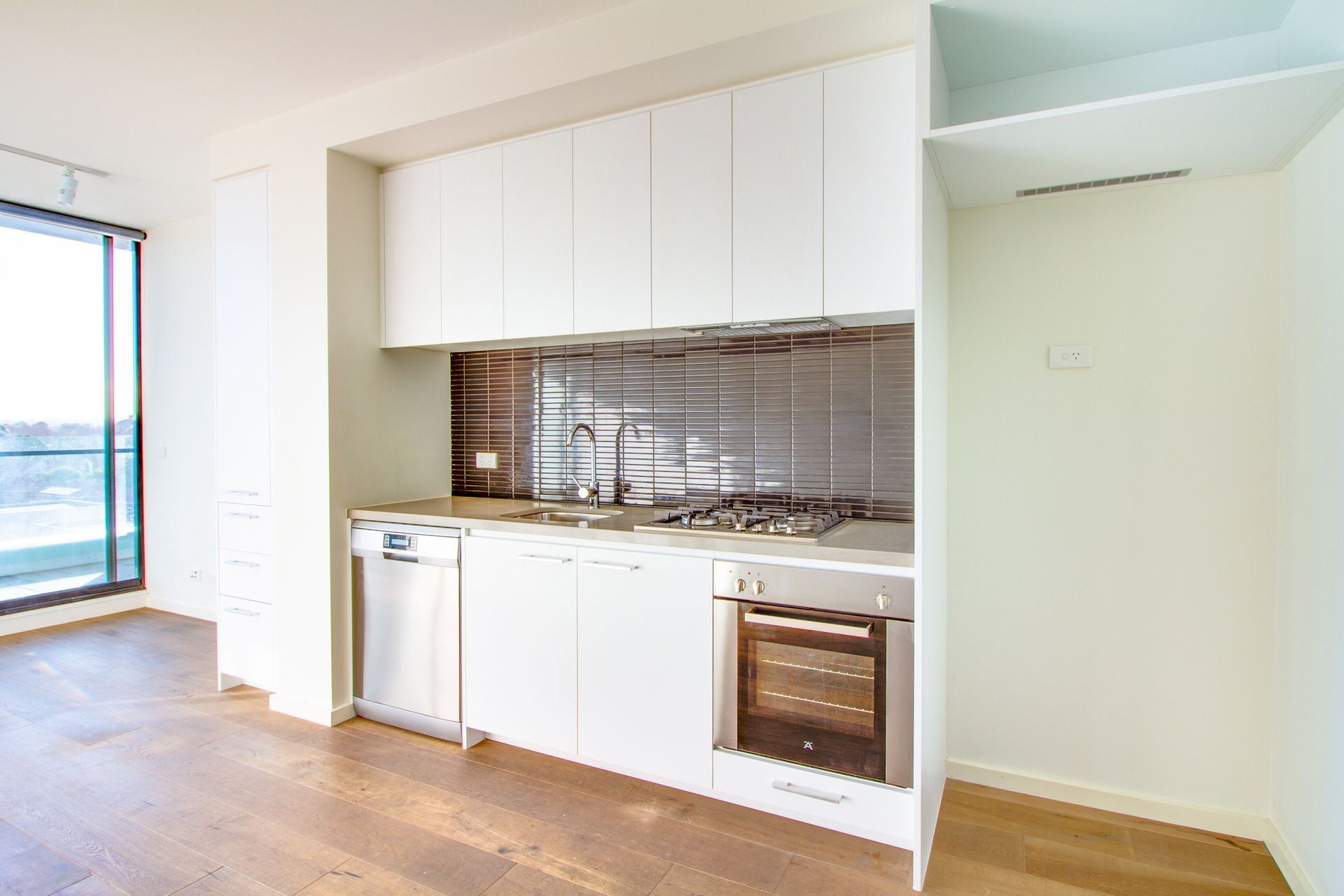 Modern white kitchen with stainless steel appliances, dark backsplash, and wooden floors.