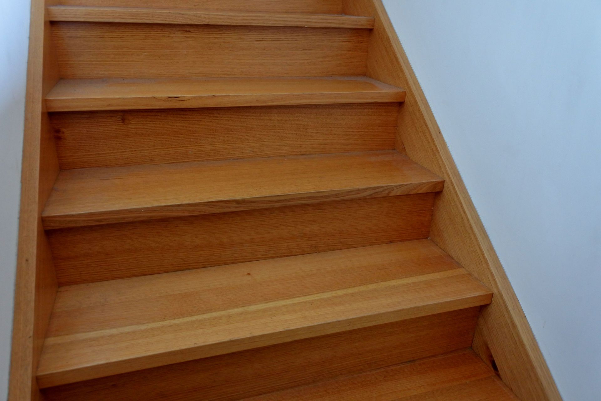 Wooden staircase with four visible steps against a white wall.