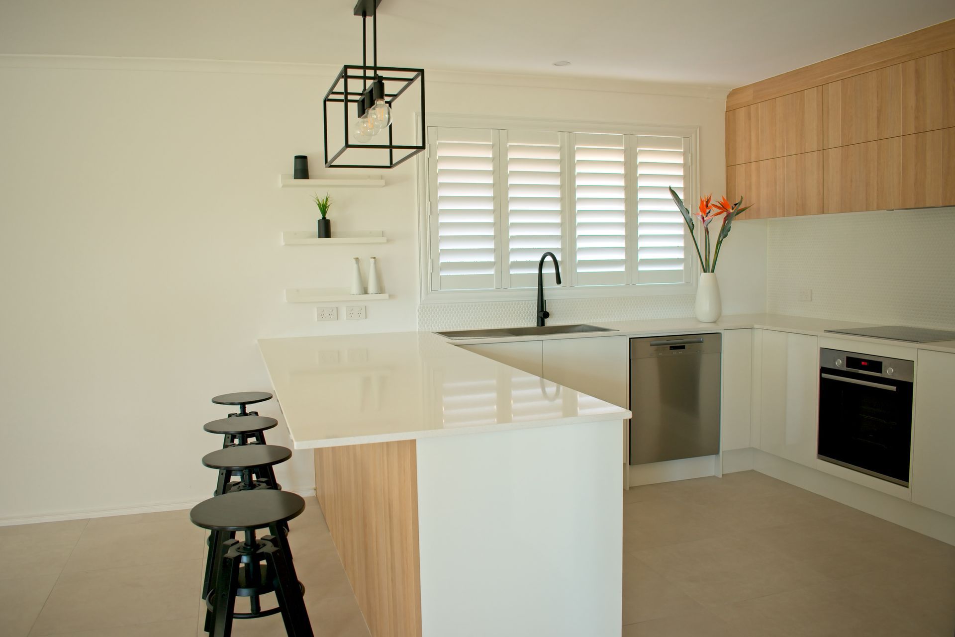Modern kitchen with white countertops, wooden cabinets, and black stools at the island.