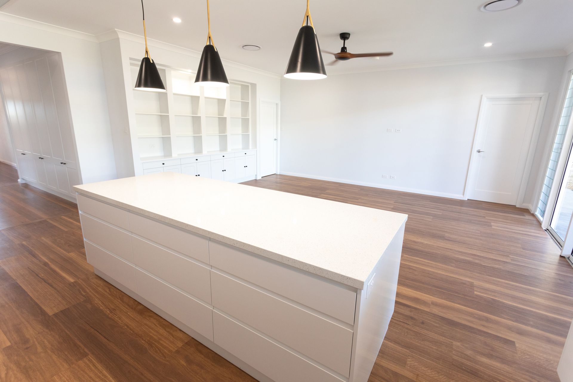 Modern kitchen with white island, dark pendant lights, and wooden floors.