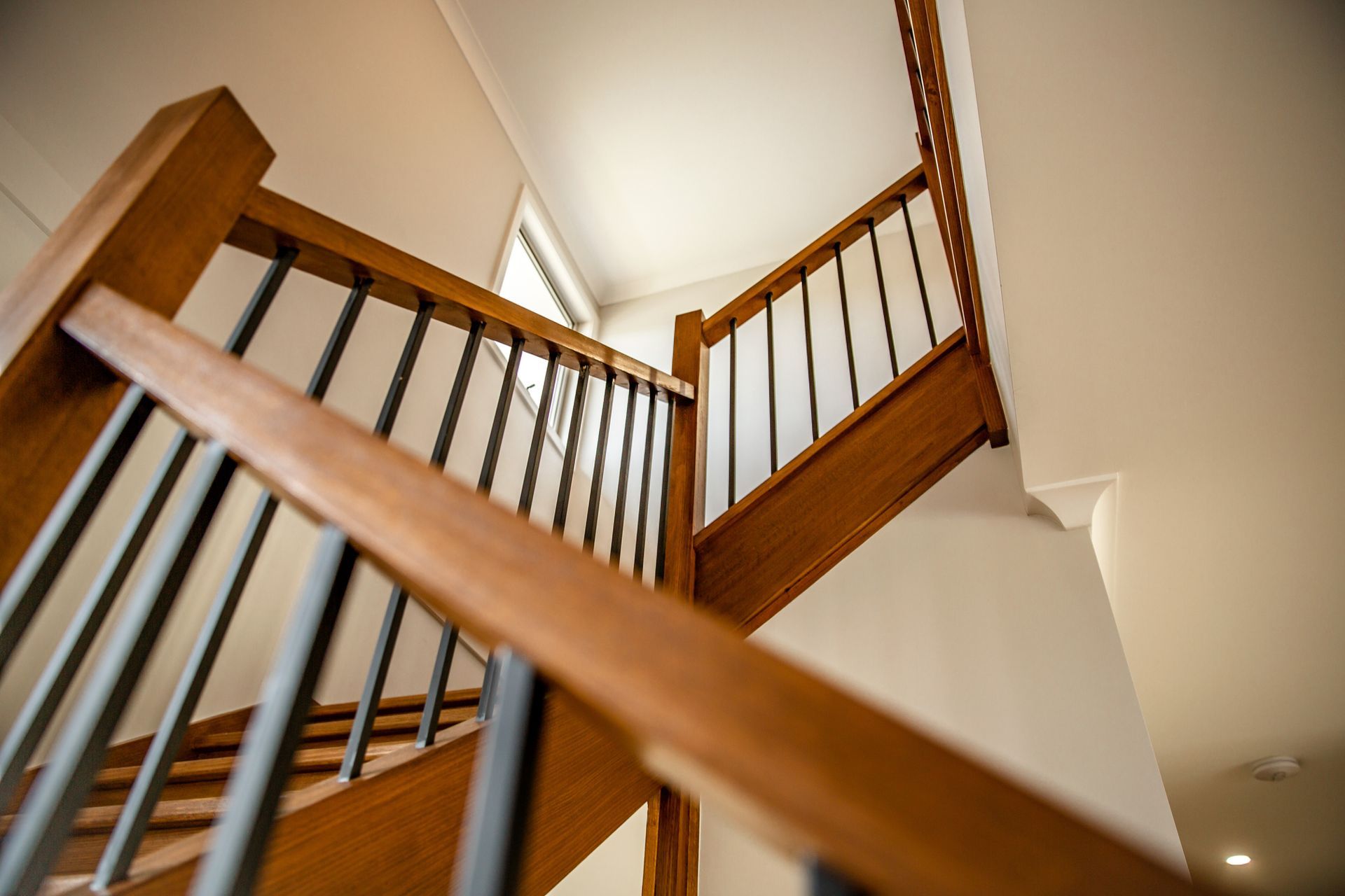 Wooden staircase with black metal balusters; the perspective is from below.