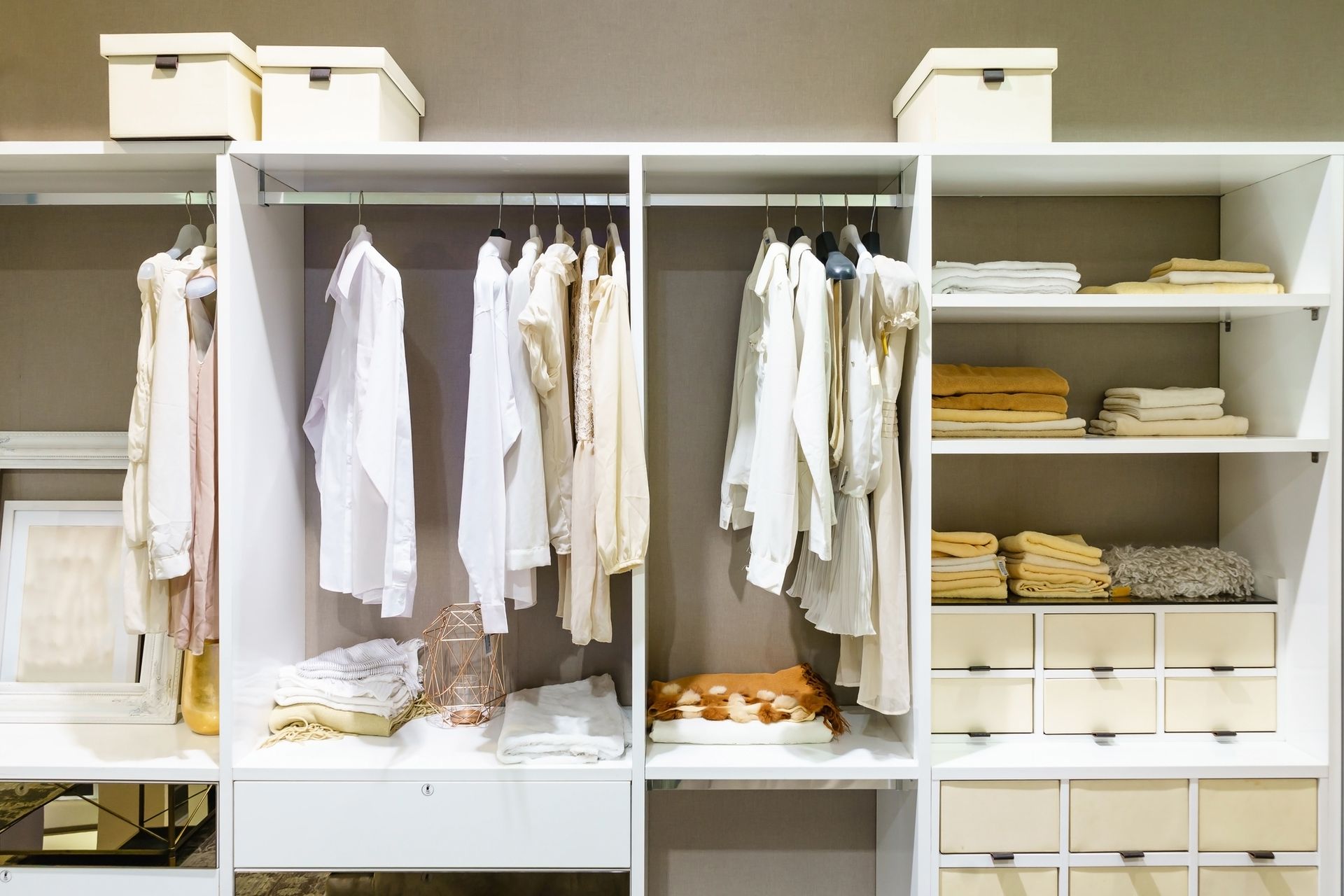 Organized white closet with hanging clothes, shelves, and storage boxes.