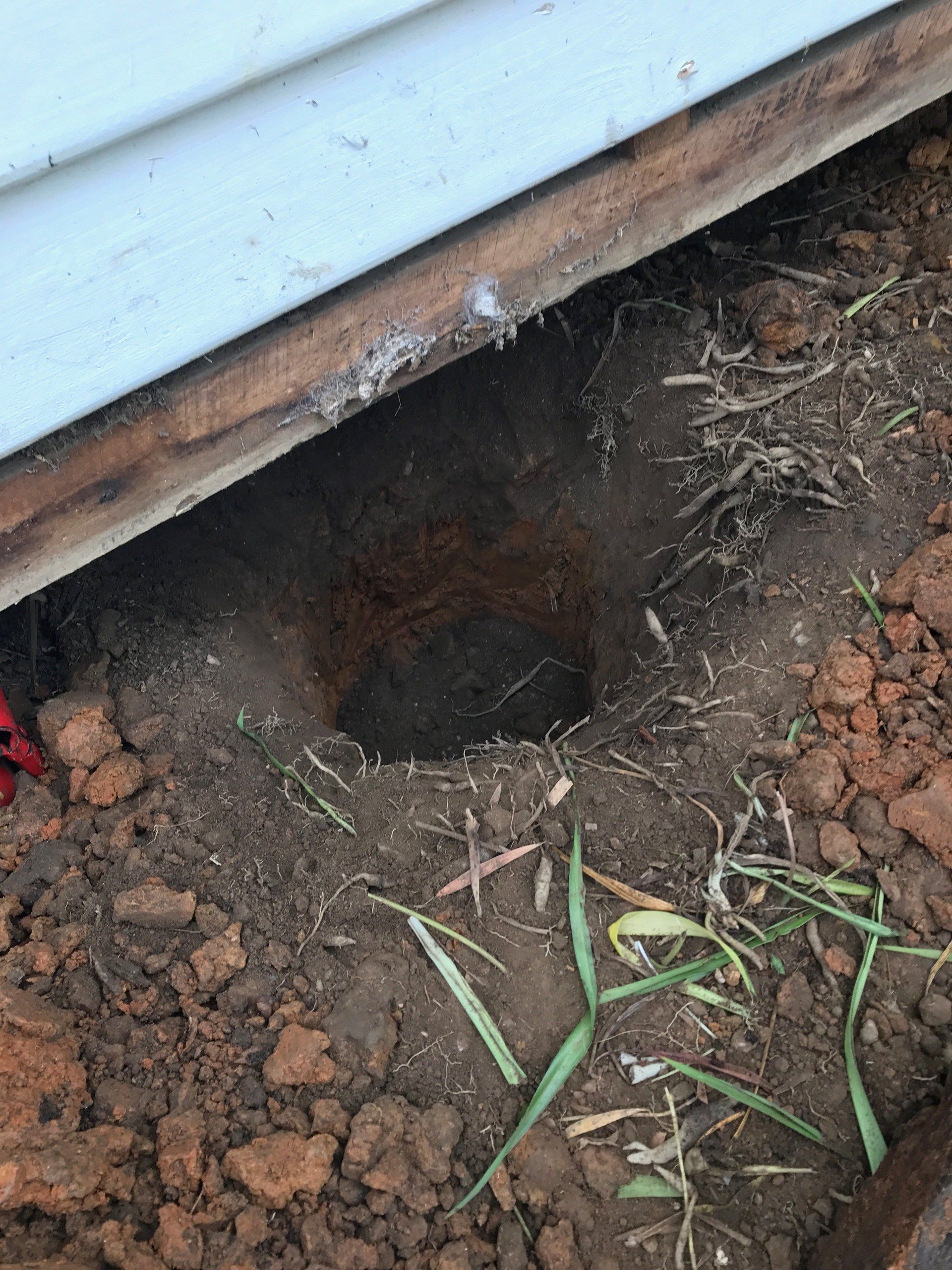 A hole in the ground under a house with grass growing out of it.