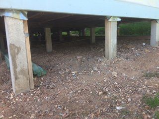 The underside of a house with concrete pillars and a lot of dirt.
