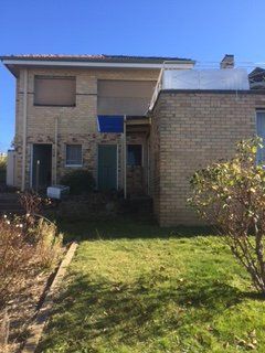 A large brick house with a blue tarp on the roof is sitting on top of a lush green lawn.