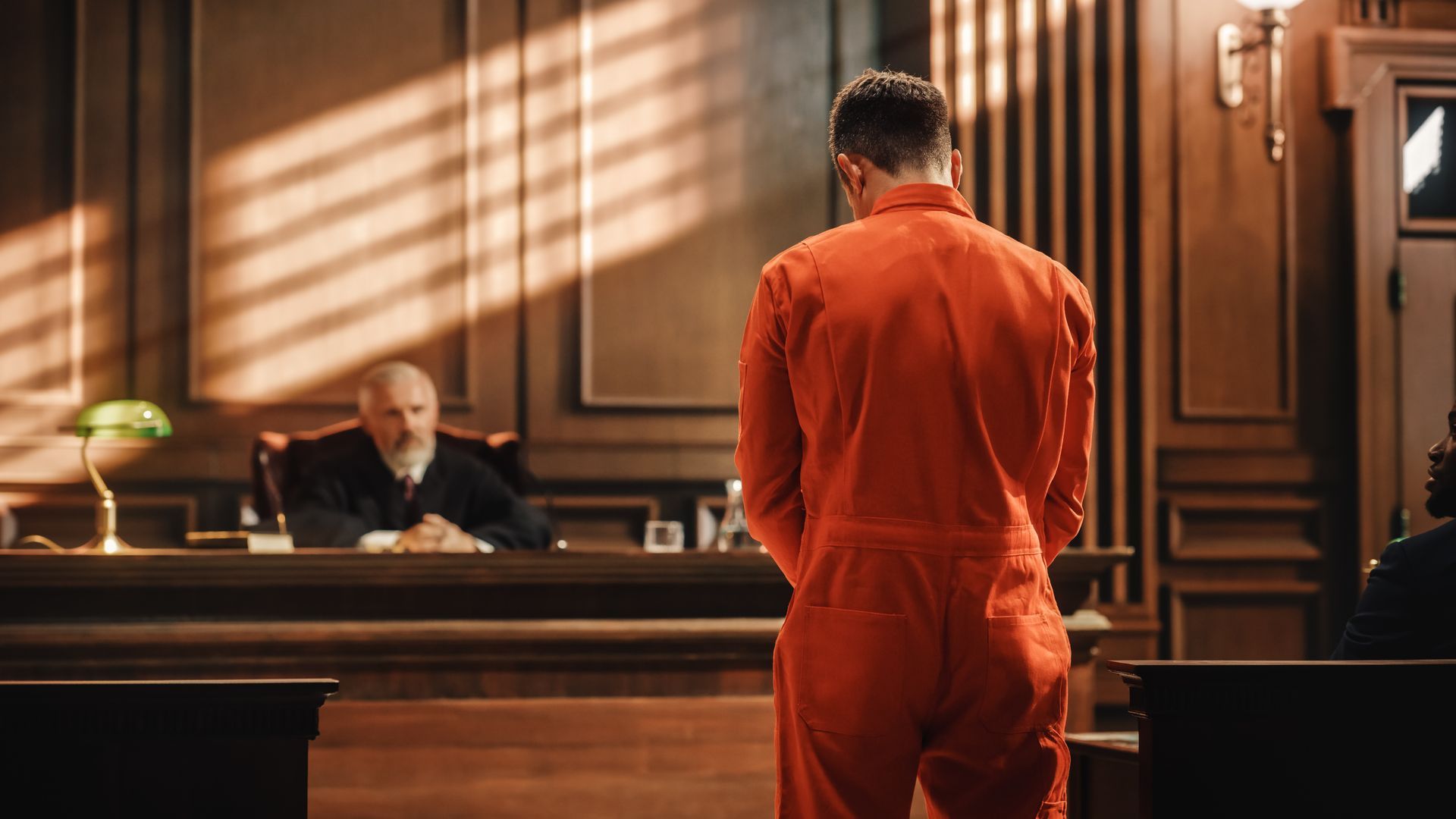 A man in a red jumpsuit is standing in front of a judge in a courtroom.