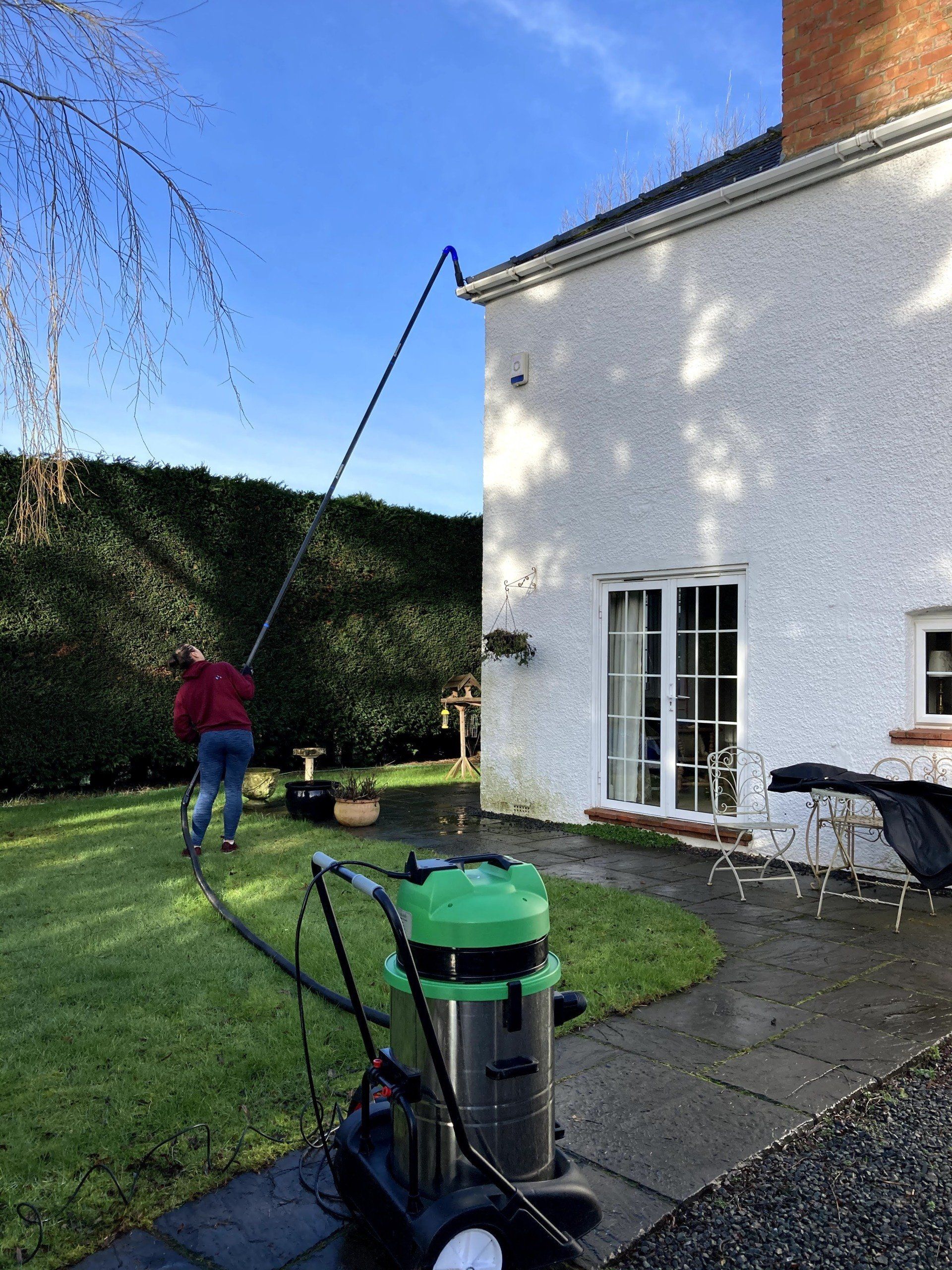 A man is cleaning the side of a house with a vacuum cleaner.