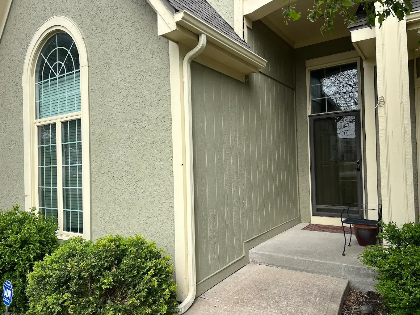 Light green stucco home exterior with a large arched window, vertical siding, and a covered front entryway.