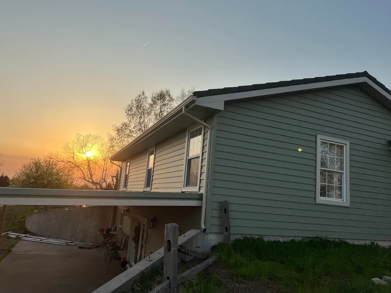 A side view of a light green house at sunset, with a concrete walkway extending from the lower level over a grassy slope.
