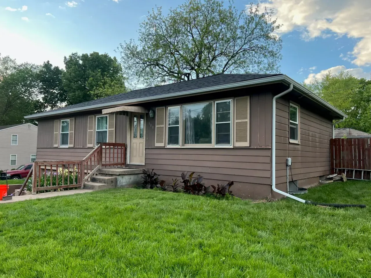 A brown, single-story ranch house with a front porch, wood siding, and light-colored shutters on a grassy lot.