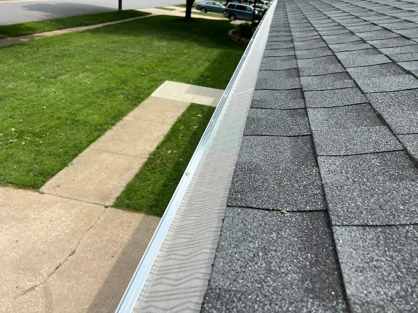 A close-up, high-angle view of a gray shingled roof with a silver metal gutter guard installed along the edge.