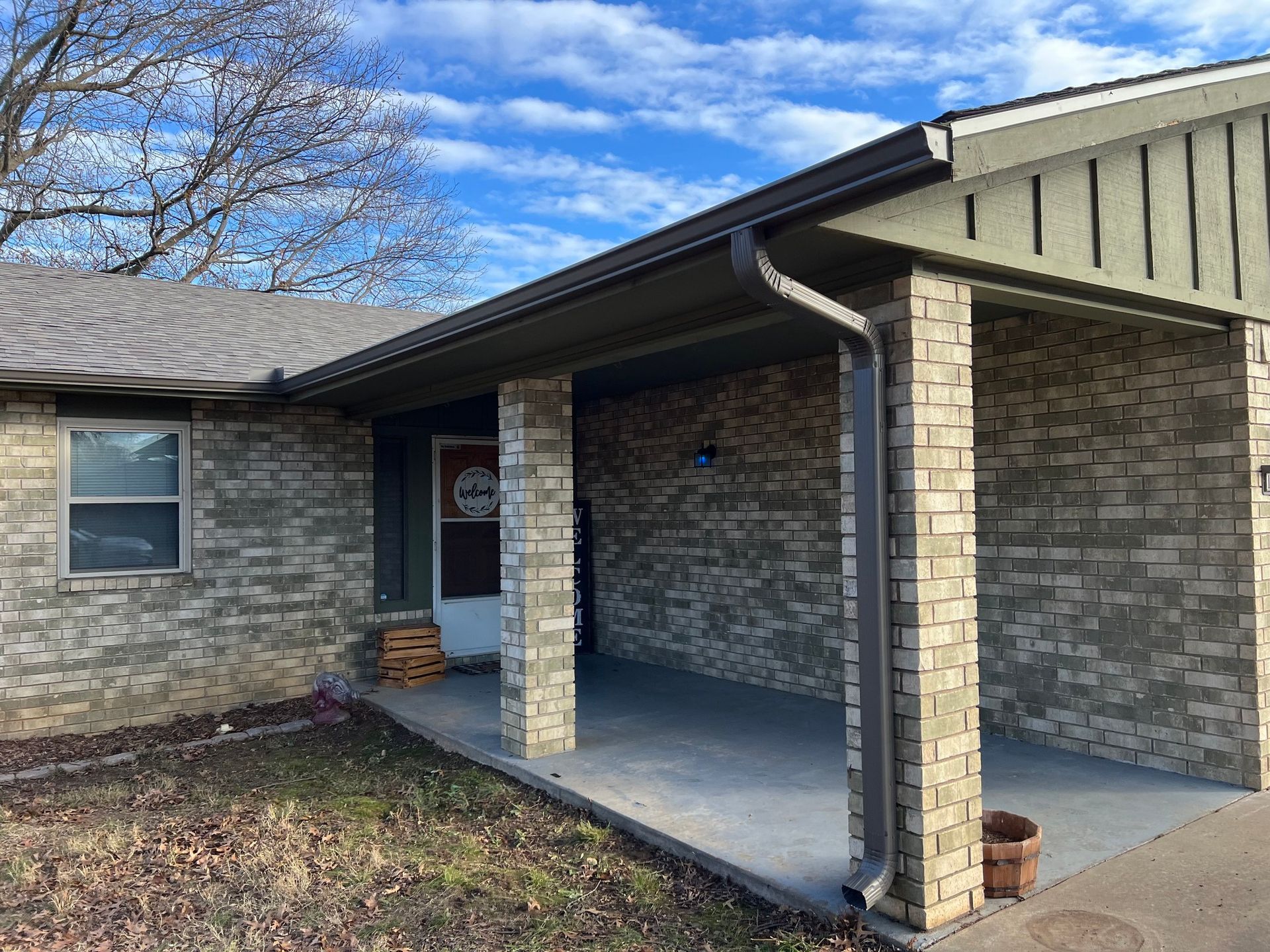 A single-story brick house with a covered front porch and gray siding, featuring a window and a front door.