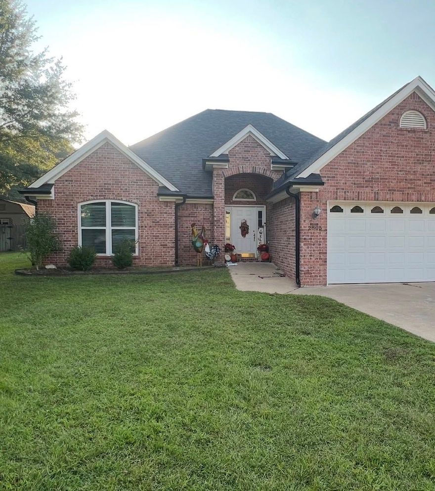 A single-story brick house with a dark shingle roof, a white garage door, and a front lawn under a clear sky.