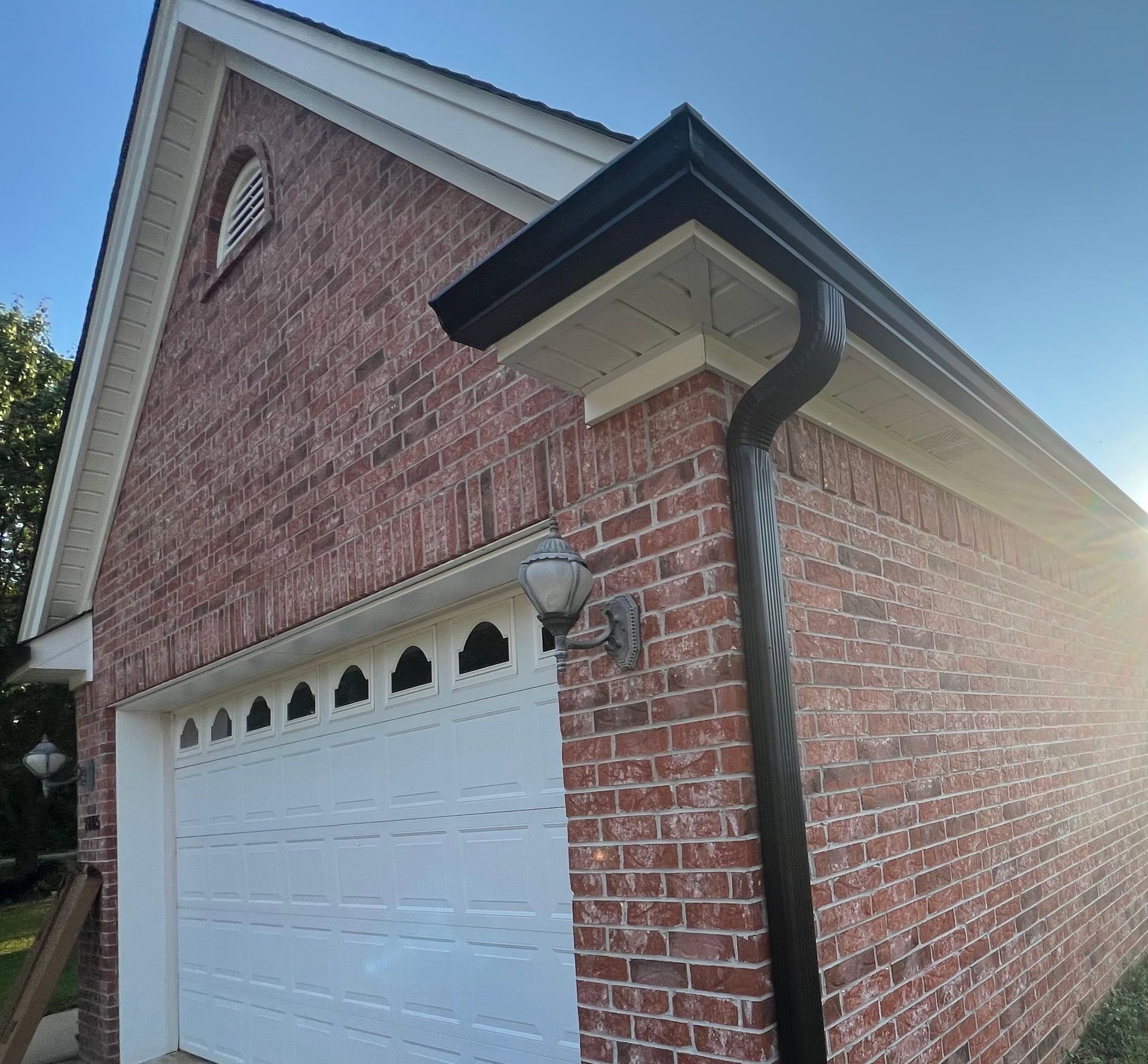 A brick garage exterior with a white door, a black gutter downspout, and an outdoor light fixture under the roof overhang.