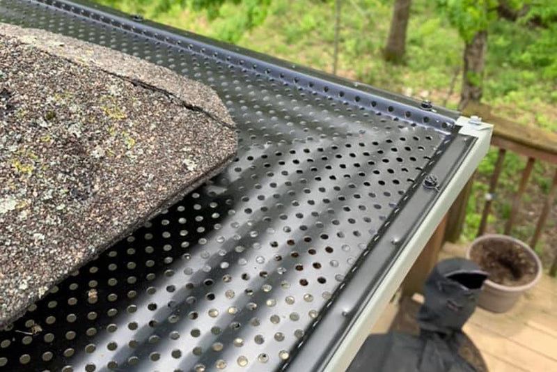 Black metal gutter guard installed over a white rain gutter along the edge of an asphalt shingle roof.
