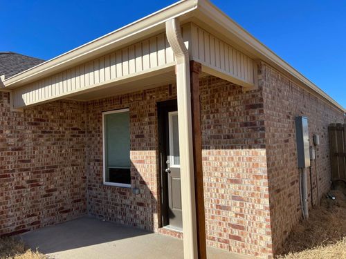 A brick exterior of a house featuring a covered porch, a single window, and a door under a clear blue sky.