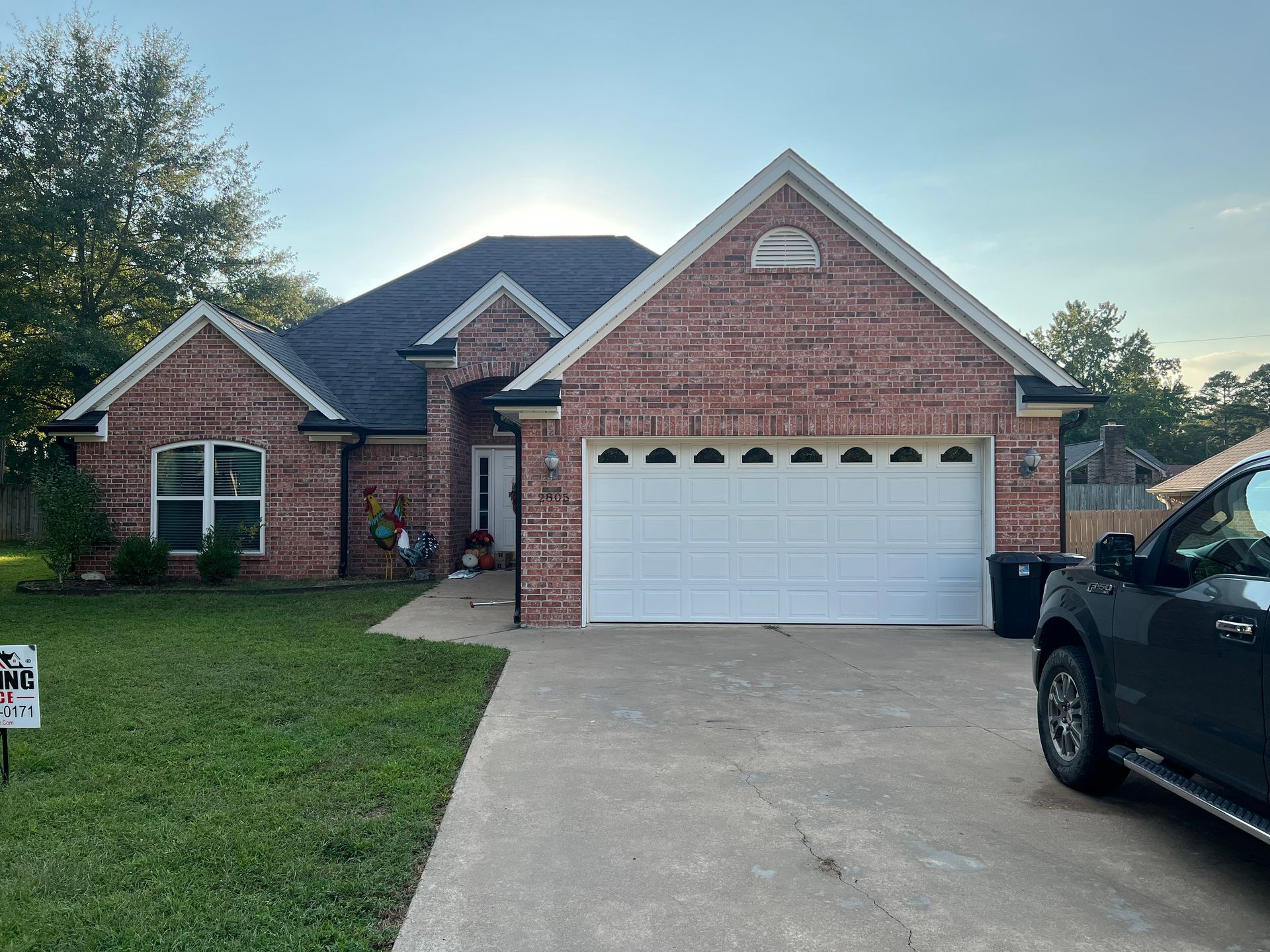 A brick, single-story suburban house with a two-car garage, a white front door, and a parked dark truck in the driveway.