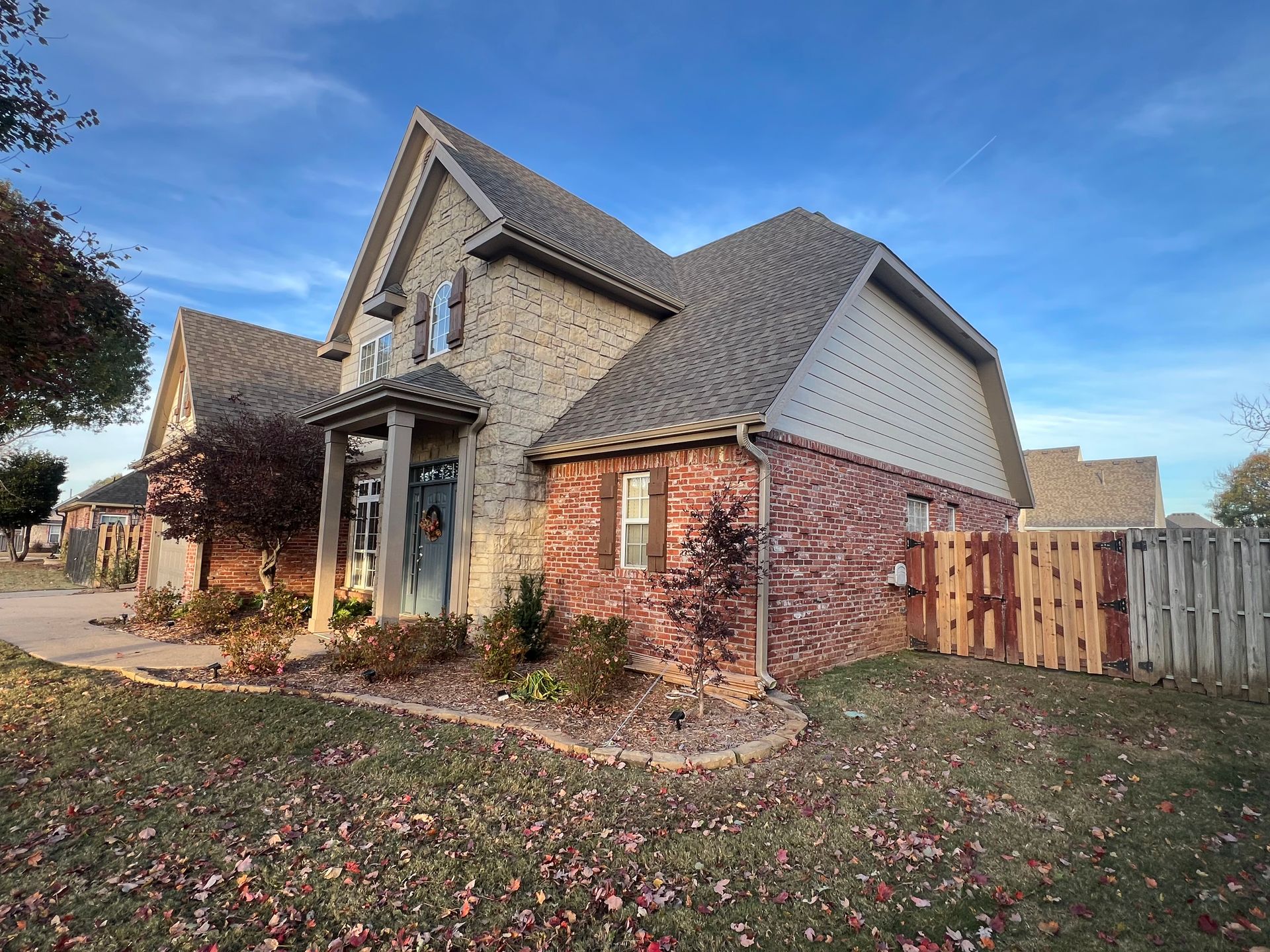 A two-story house with a brick exterior and a steeply pitched shingled roof, set in a yard covered in fallen leaves.